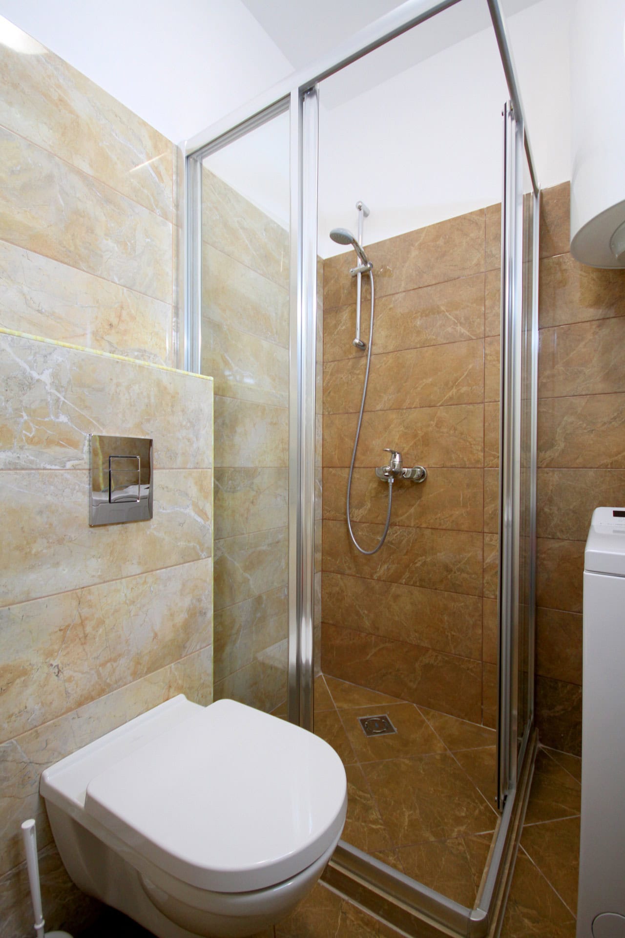 Modern bathroom in an apartment in Bečići, Montenegro: shower cabin, wall-hung toilet, and beige tiles.