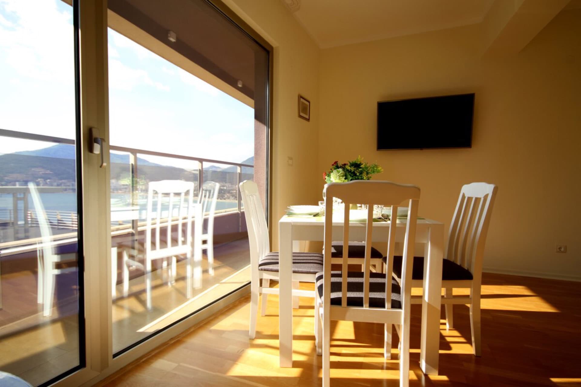 Living room with dining area and panoramic sea view in an apartment in Becici, Montenegro. Light furniture and a terrace.
