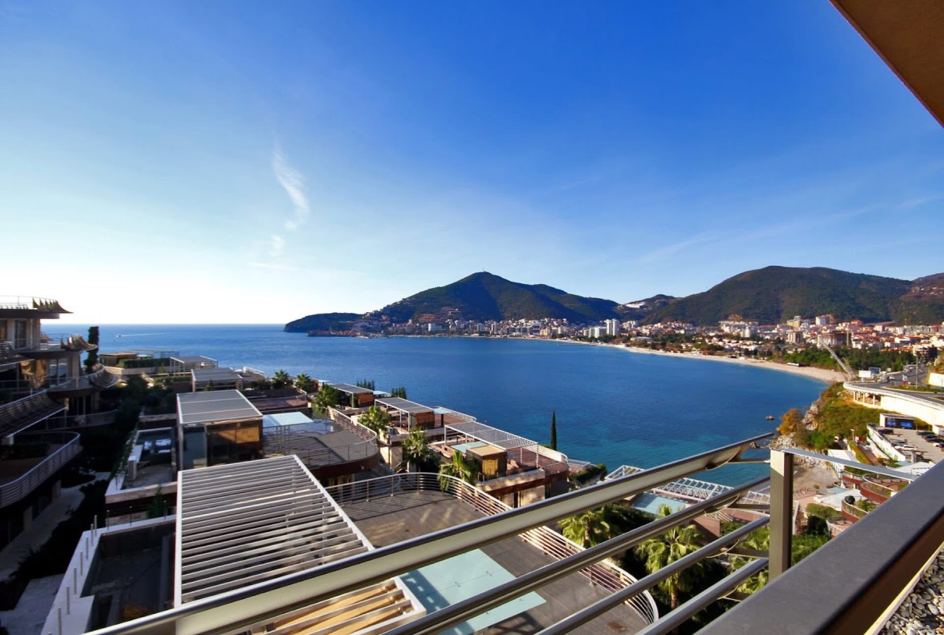 Panoramic view from the apartment balcony in Bečići, Montenegro: sea, beach, and mountains in a luxury residential complex with terraces.