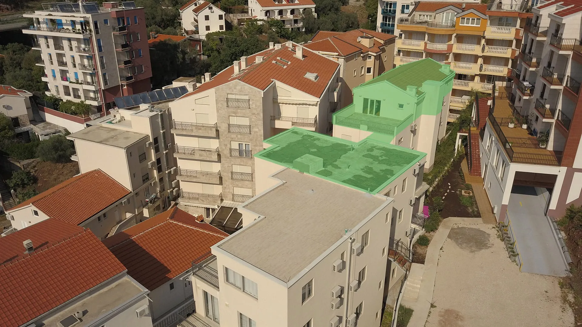 Aerial view of residential buildings with red tiled roofs and highlighted green flat terraces.