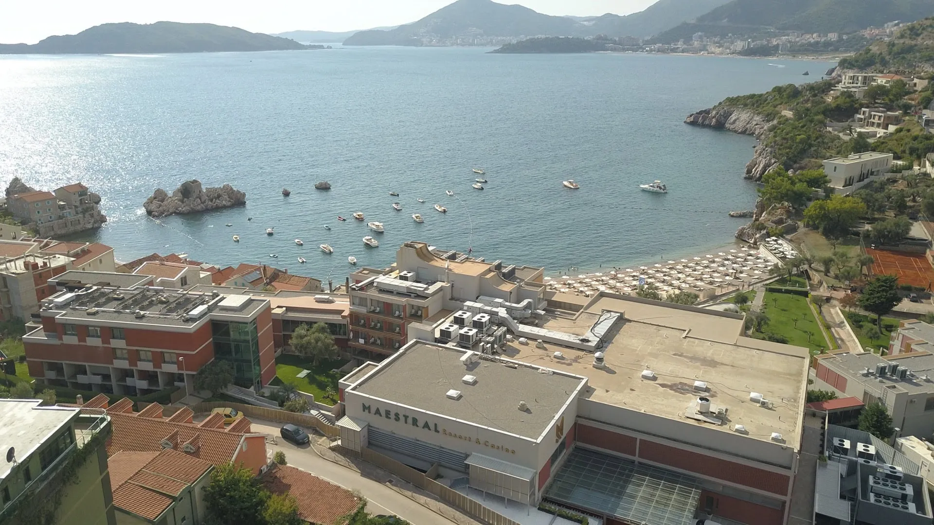 Aerial view of Maestral Resort, sea with boats, beach umbrellas, and surrounding mountains.