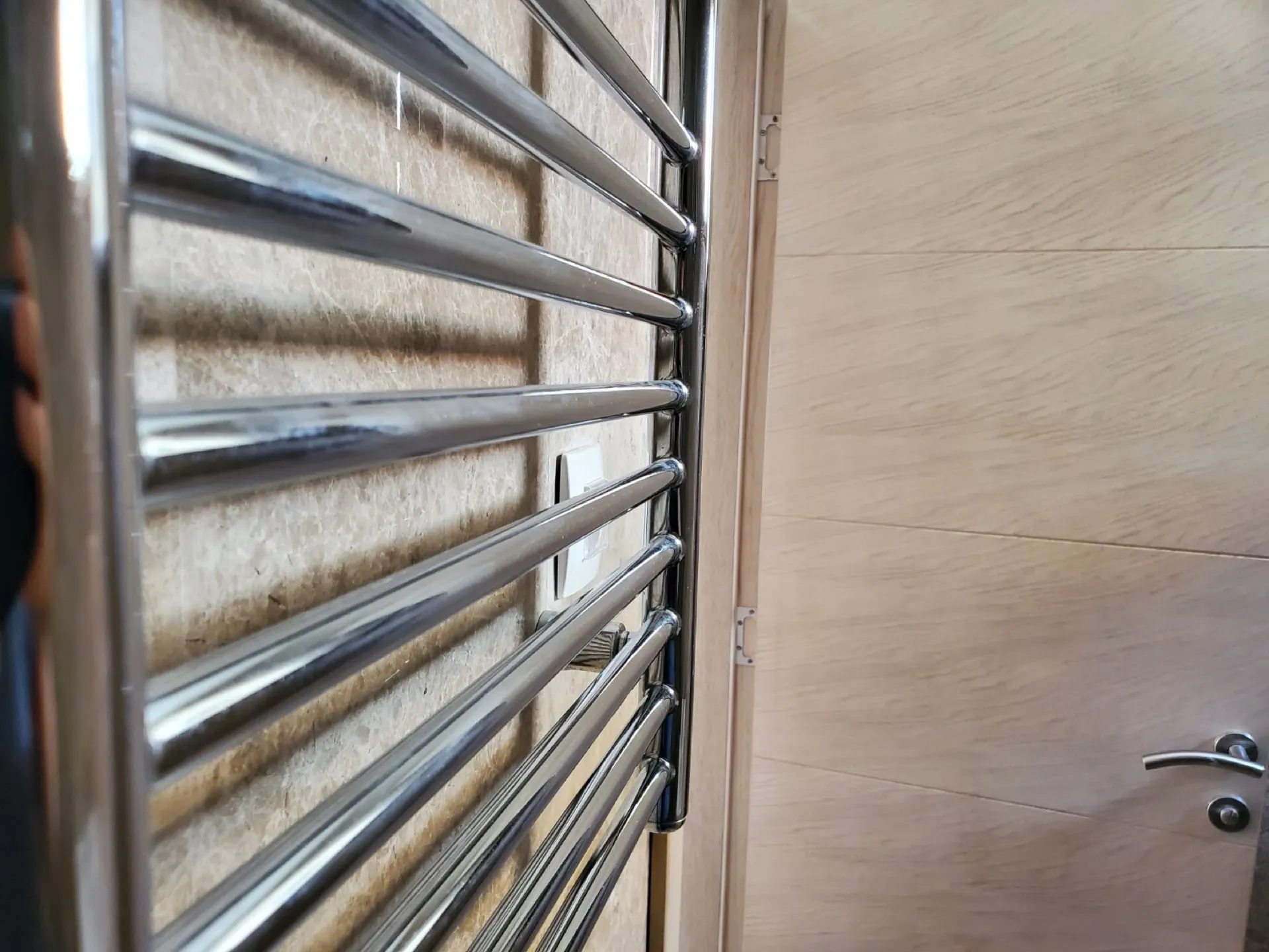 Chrome heated towel rail mounted on a tiled wall next to a light wood door.