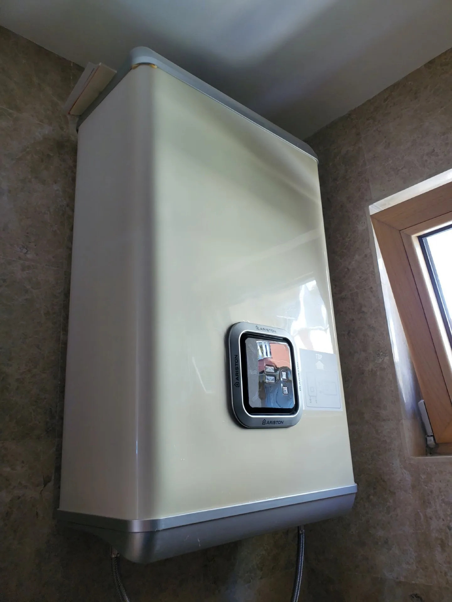 Wall-mounted Ariston boiler unit against a tiled wall next to a wooden window frame.