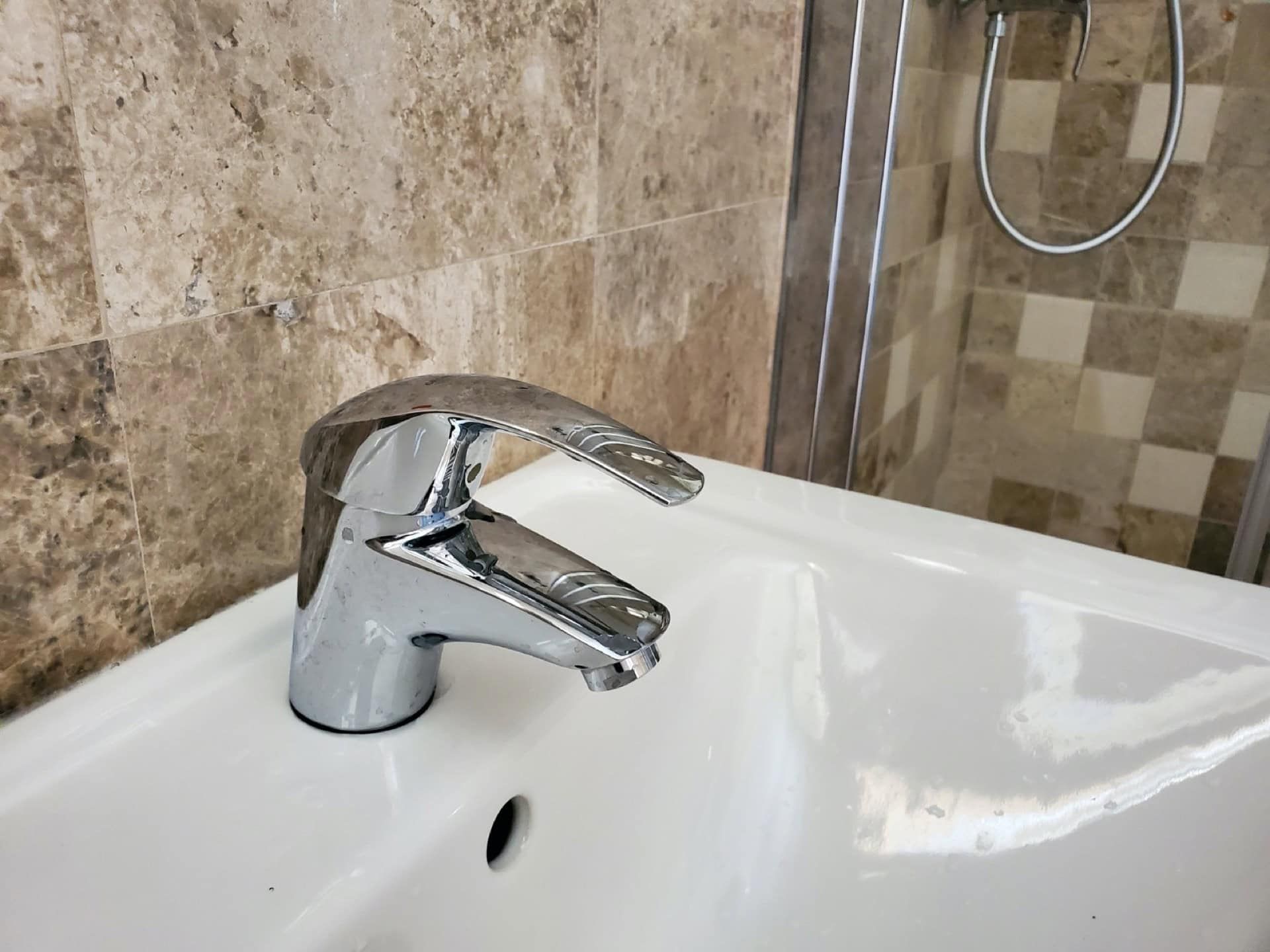 Modern faucet and white sink in the penthouse bathroom in Pržno, Montenegro, with beige stone finishes.