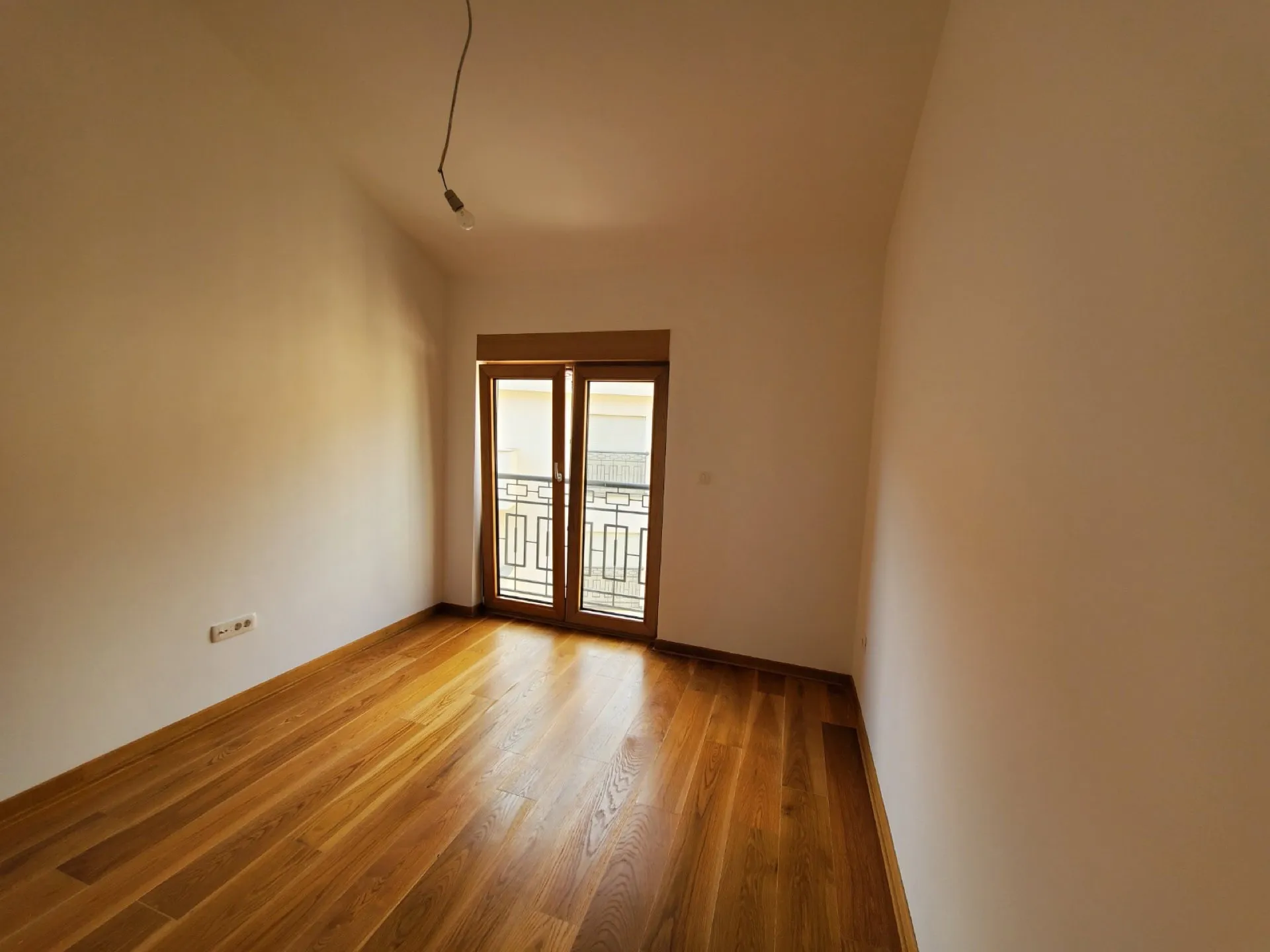 Empty room with wooden flooring and a glass door leading to a balcony.