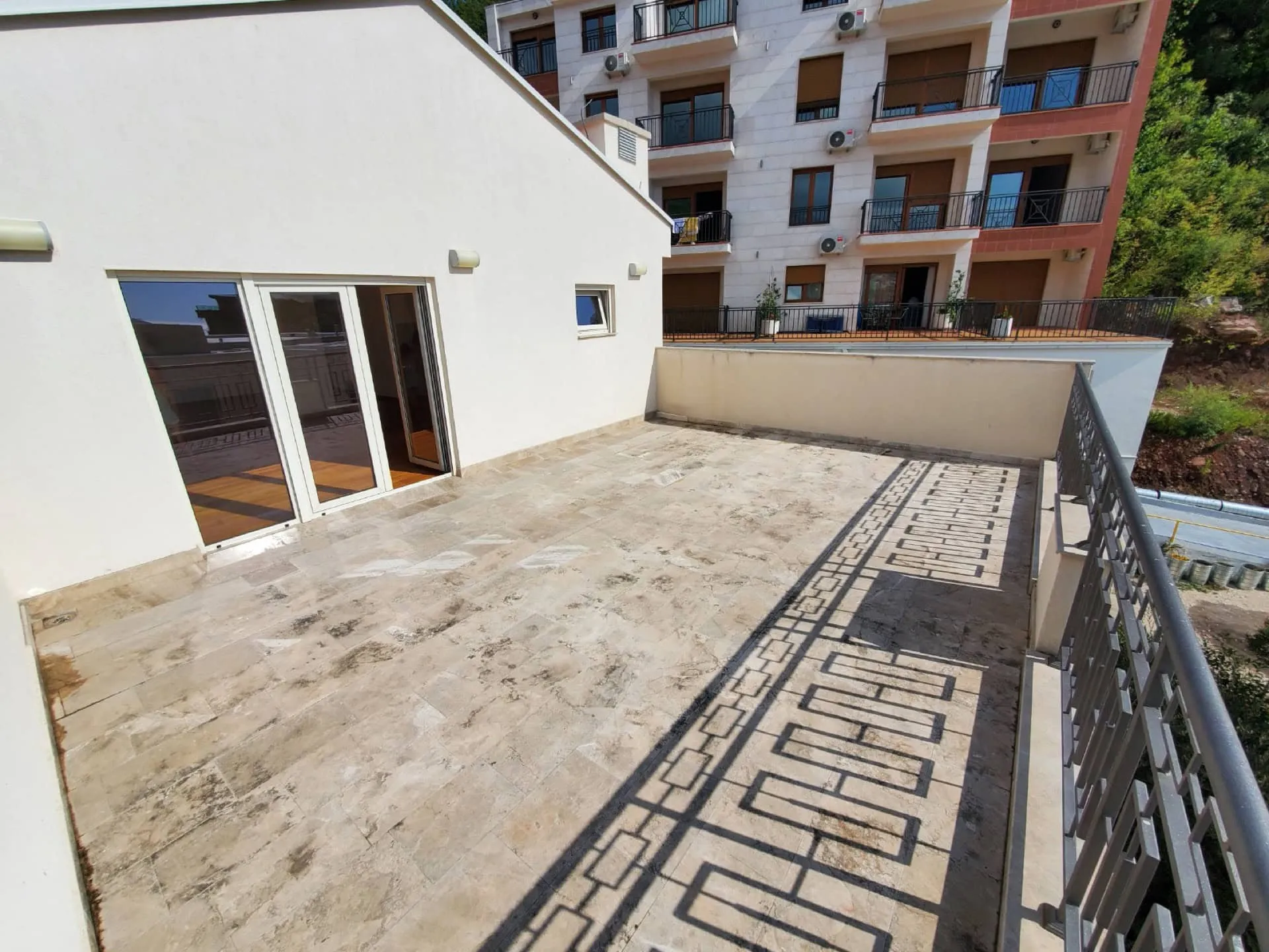 Stone balcony with metal railing and sliding glass doors overlooking a multi-story residential building.