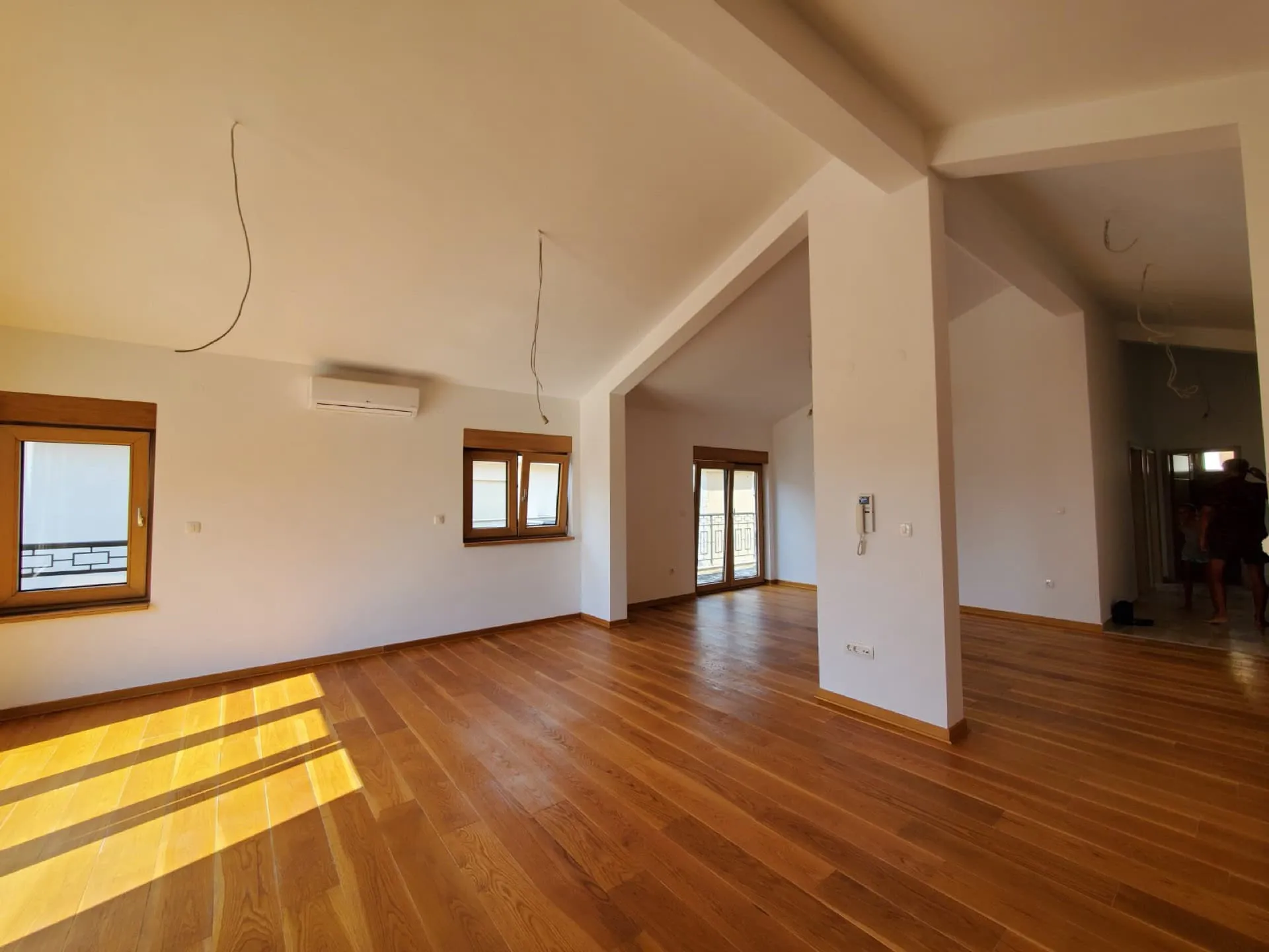 Empty room with wooden flooring, windows, AC unit, and an archway leading to a hallway.