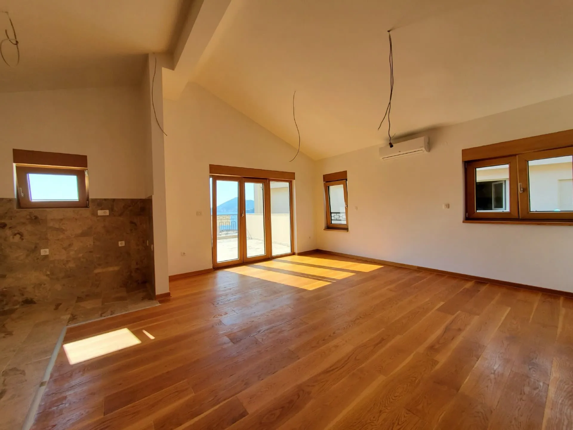 Empty room with wooden floors, high ceiling, and balcony access. A tiled wall section is visible on the left.