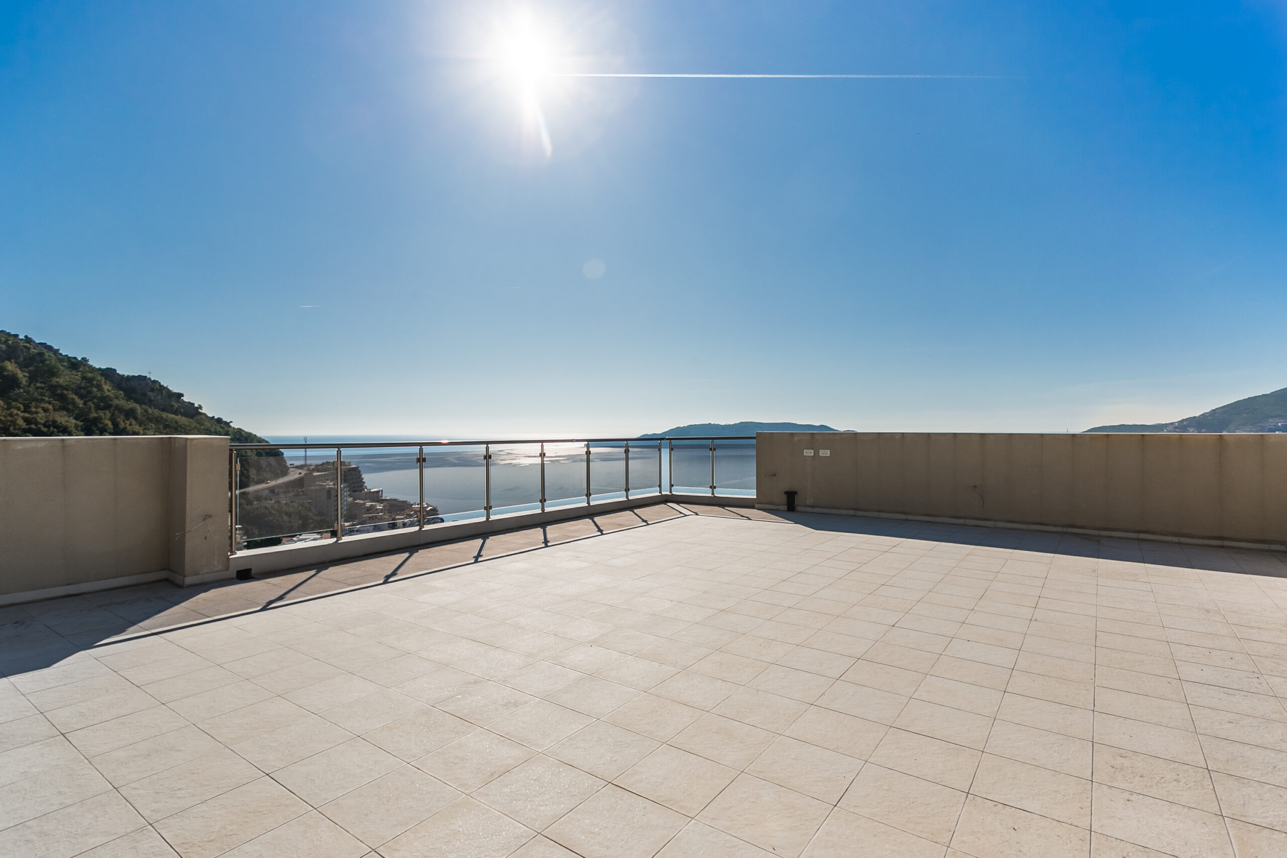 Spacious penthouse terrace in Rafailovici, Montenegro, with panoramic sea views and a glass railing.