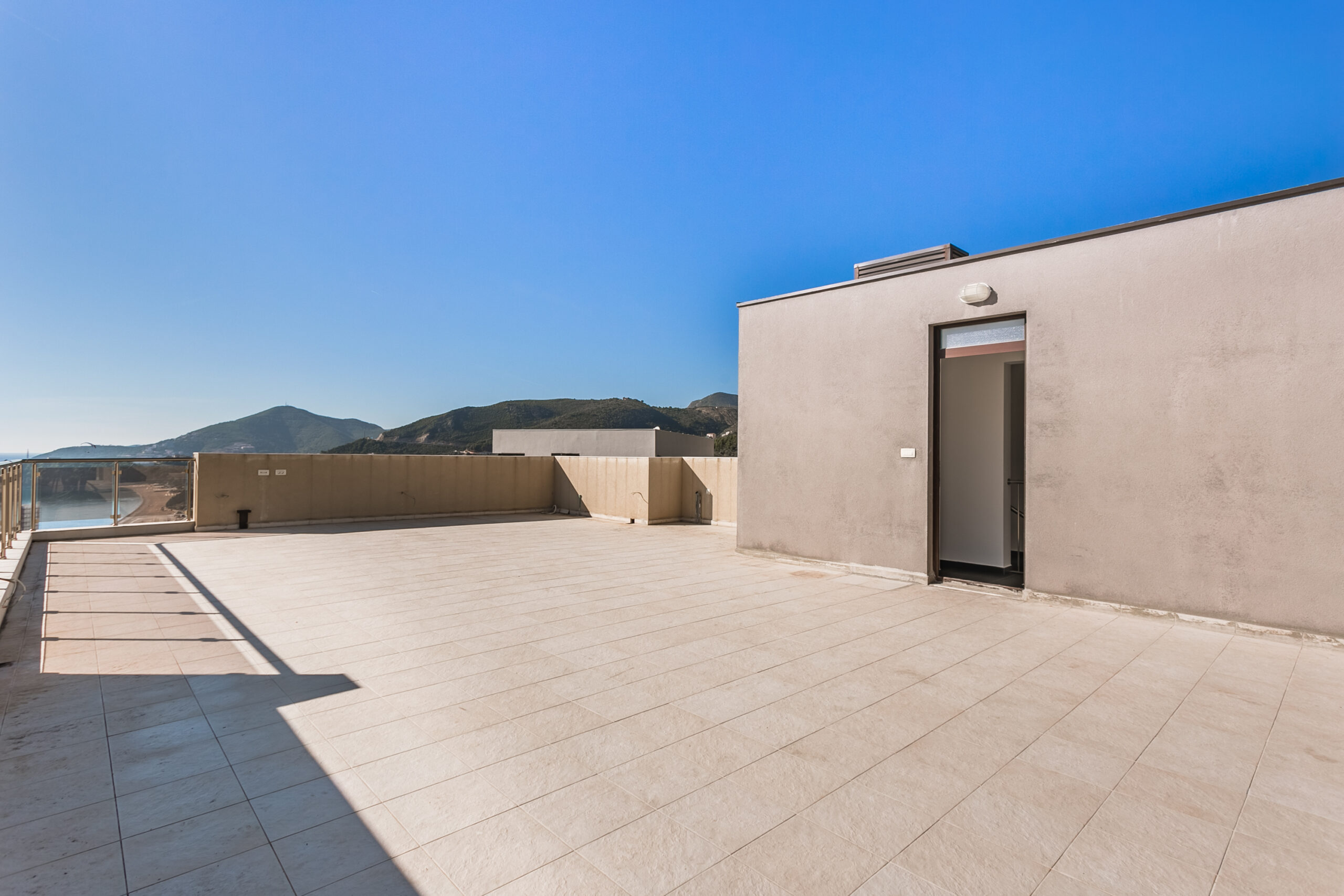 Spacious open penthouse terrace in Rafailovici, Montenegro, with sea and mountain views, paved with light-colored tiles.