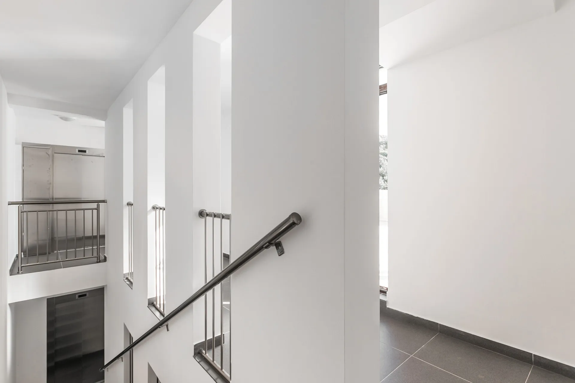 Modern staircase with metal handrail and white walls, overlooking a lower floor landing.