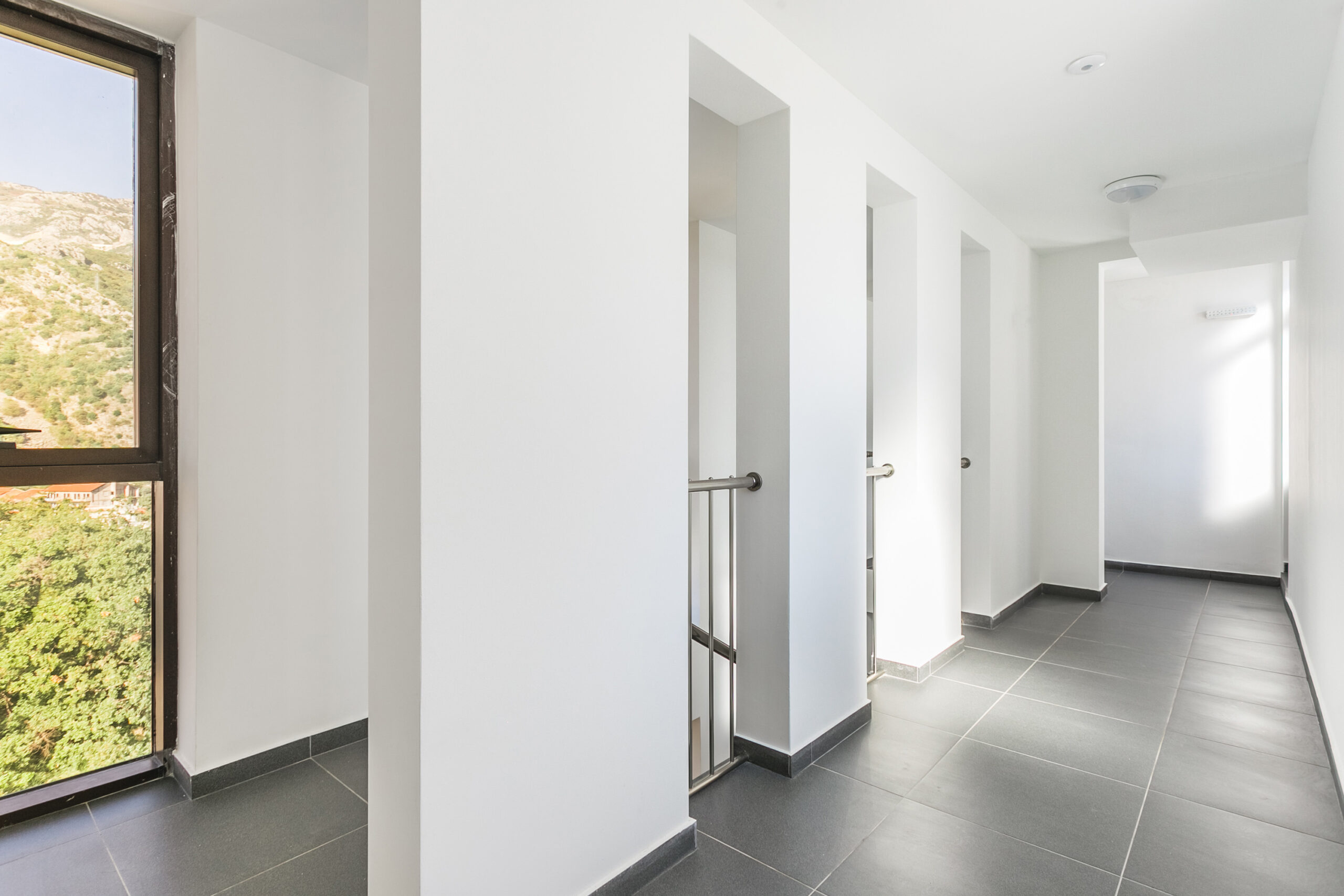 Bright penthouse hallway in Rafailovici, Montenegro, with panoramic mountain views and gray floor tiles.