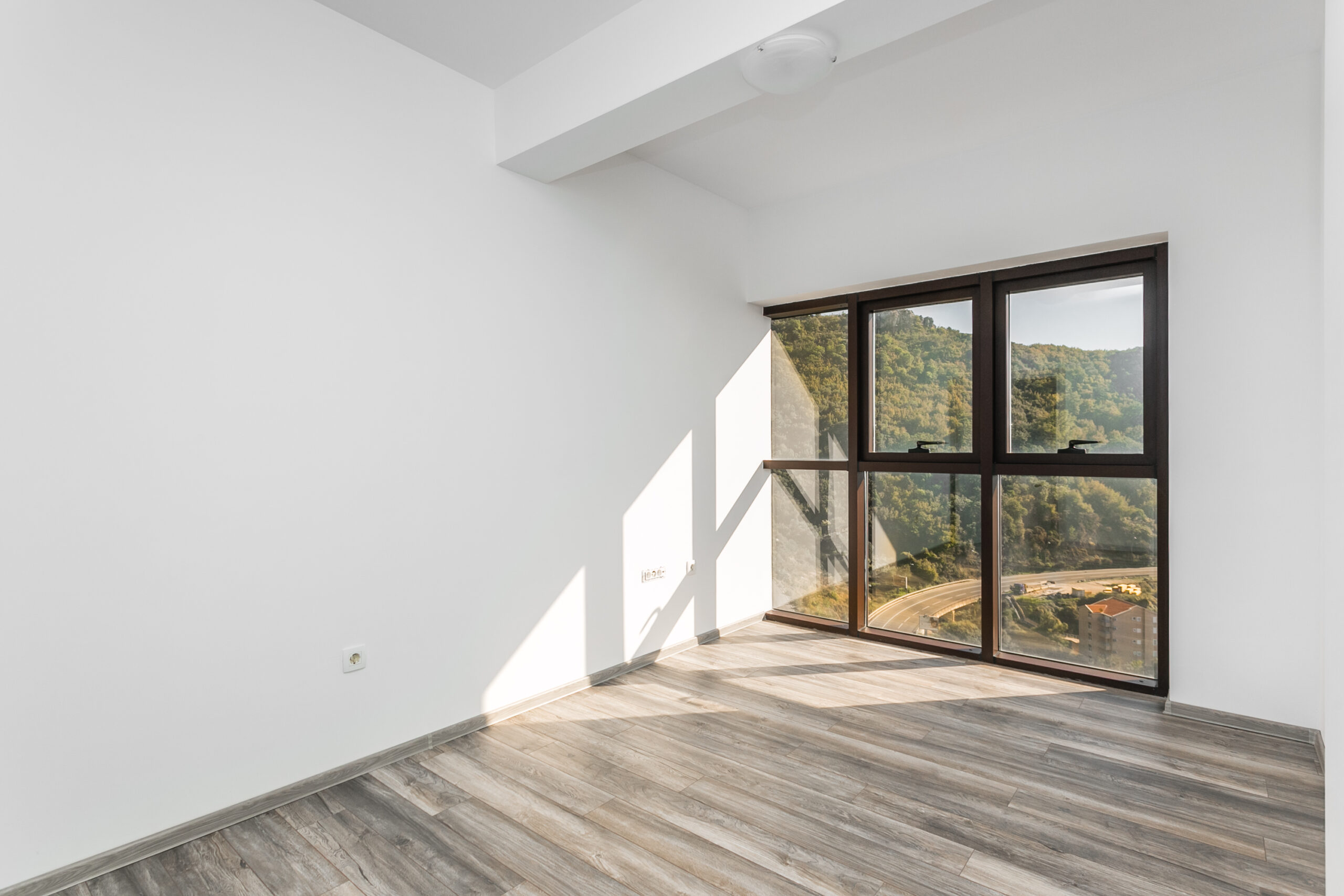 Bright living room in a penthouse, Rafailovici, Montenegro: panoramic windows with mountain views and wood-look laminate flooring.