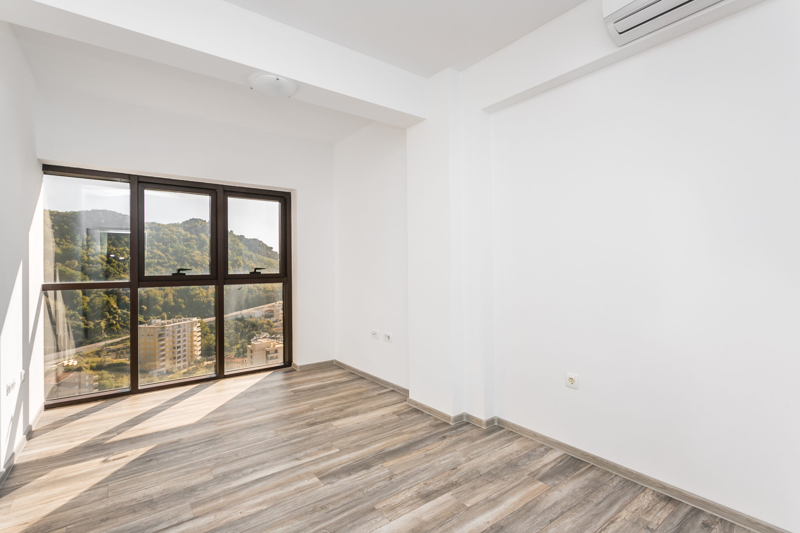 Bright living room in a penthouse in Rafailovici, Montenegro: panoramic windows with mountain views, laminate flooring, and white walls.