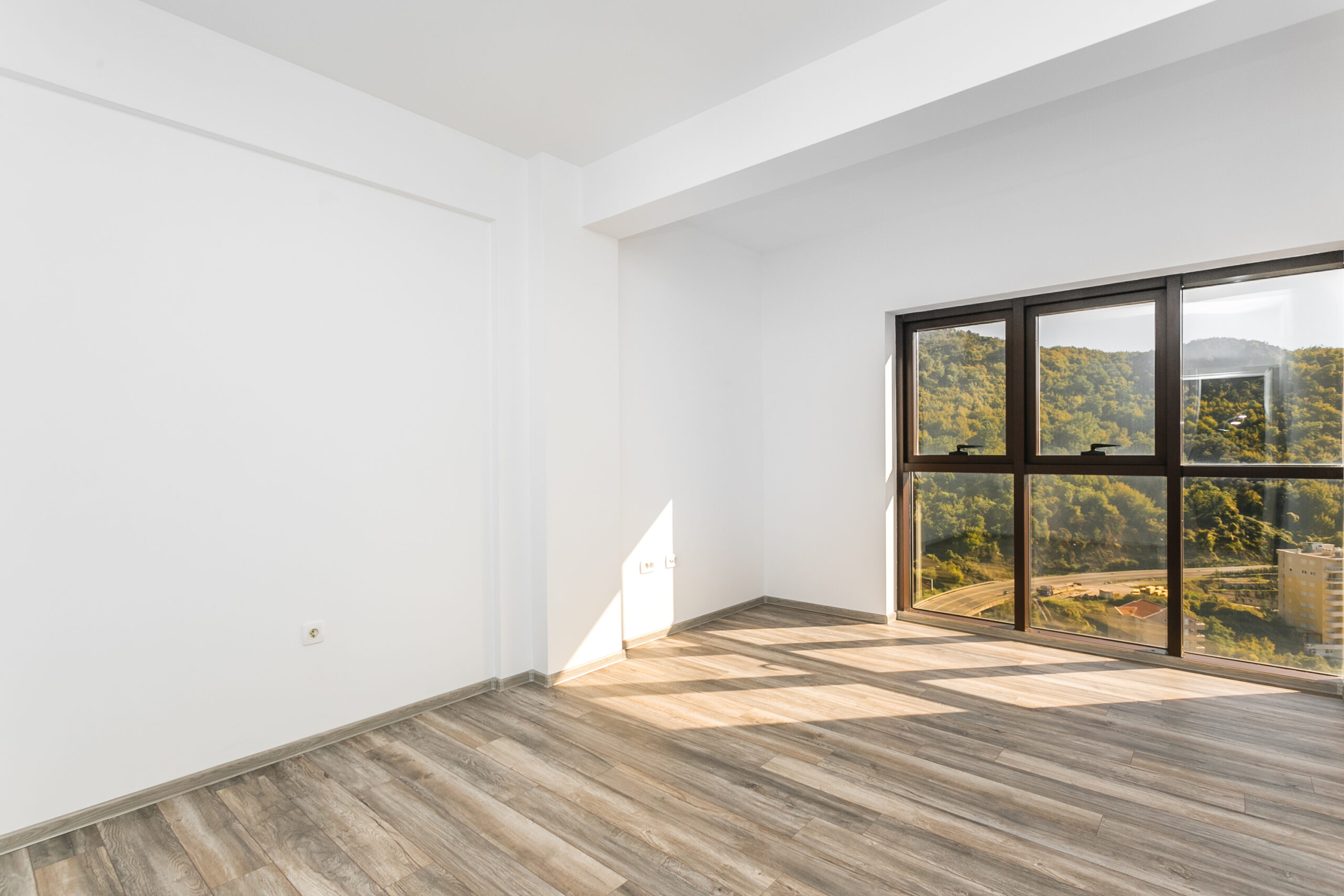 Bright living room in a penthouse, Rafailovici, Montenegro: panoramic windows with mountain views, laminate flooring, white walls.