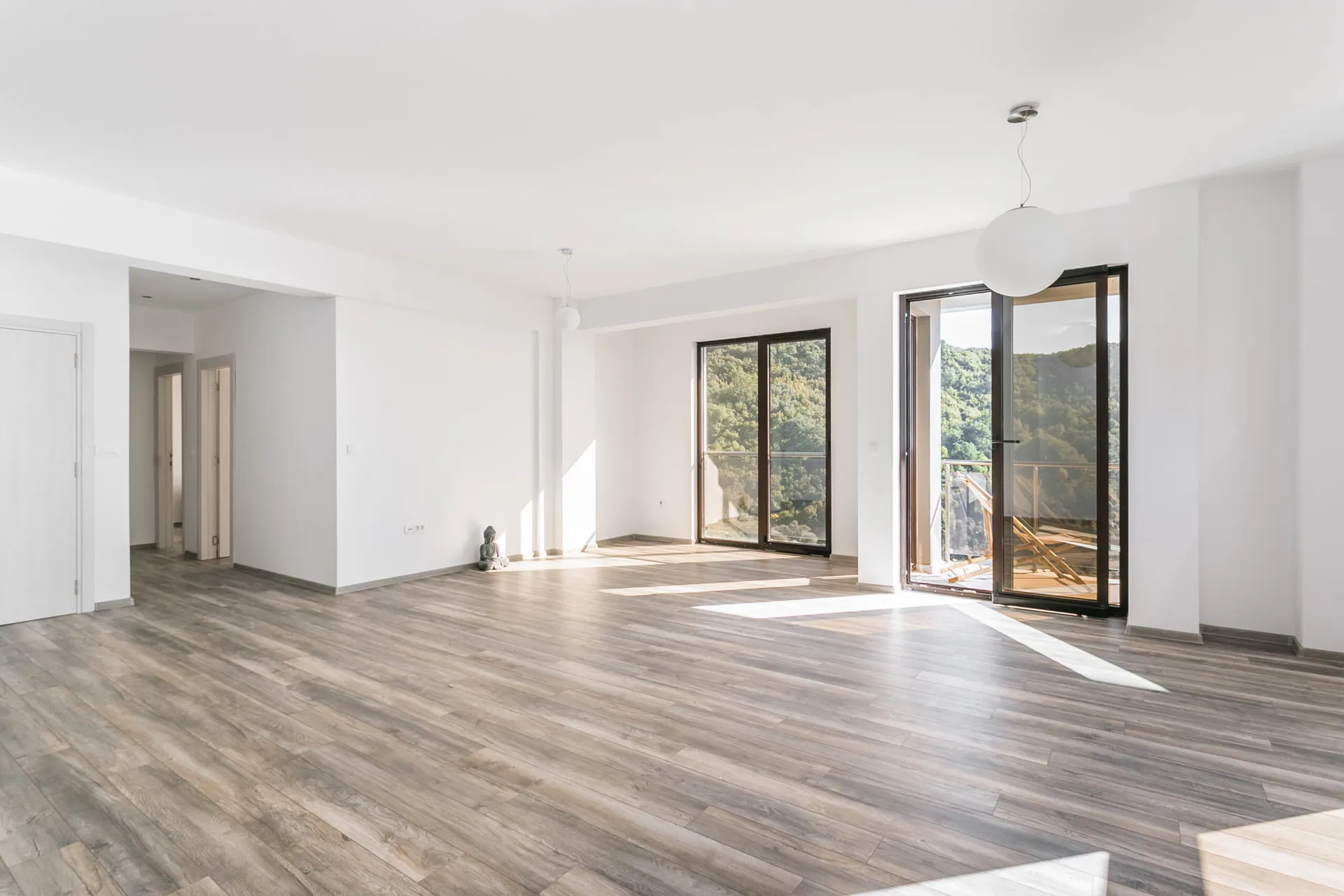 Empty bright room with wood flooring, white walls, pendant lights, and glass doors leading to a balcony.
