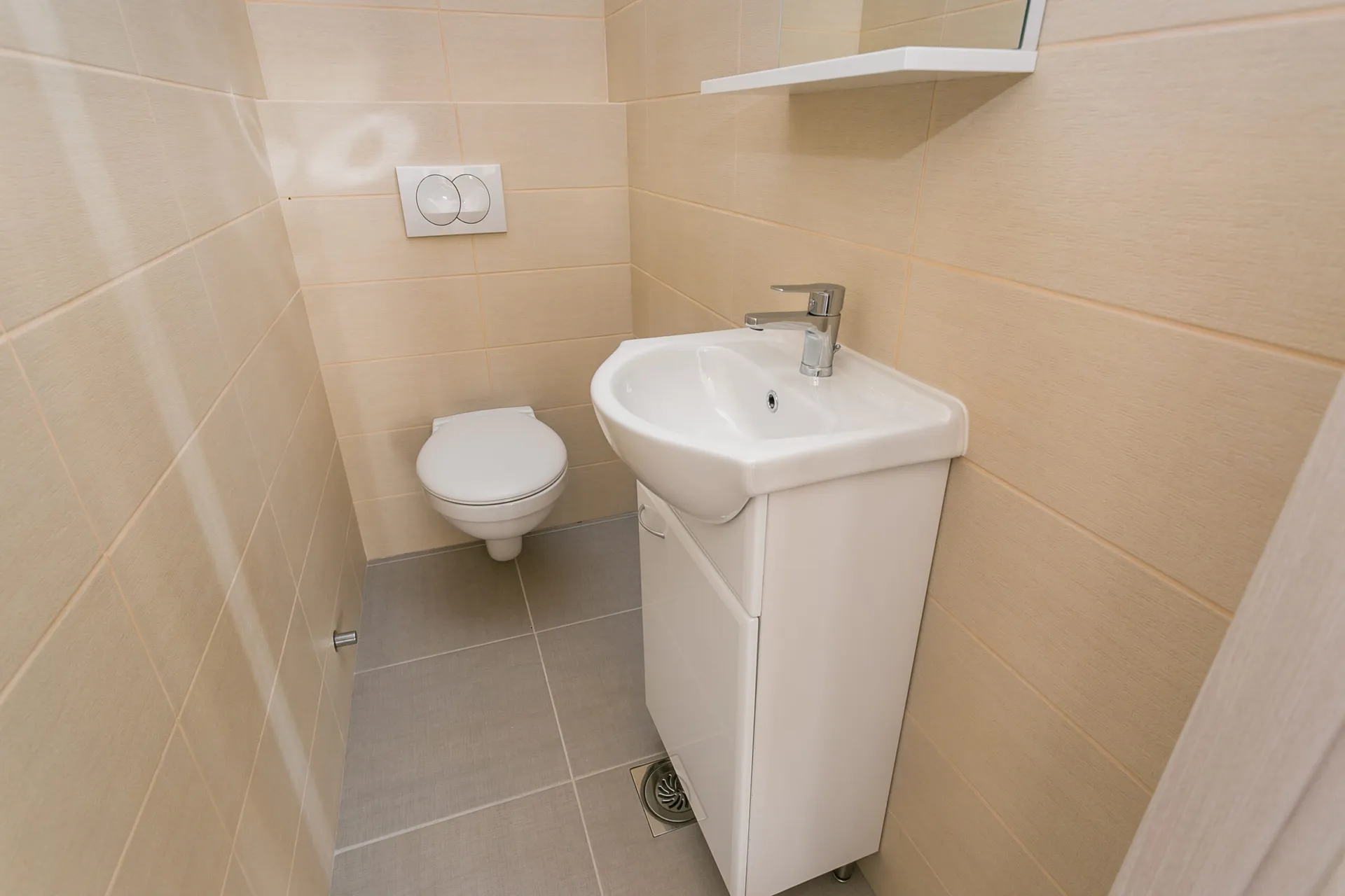 Small bathroom featuring a white toilet, vanity sink with cabinet, and beige wall tiles.