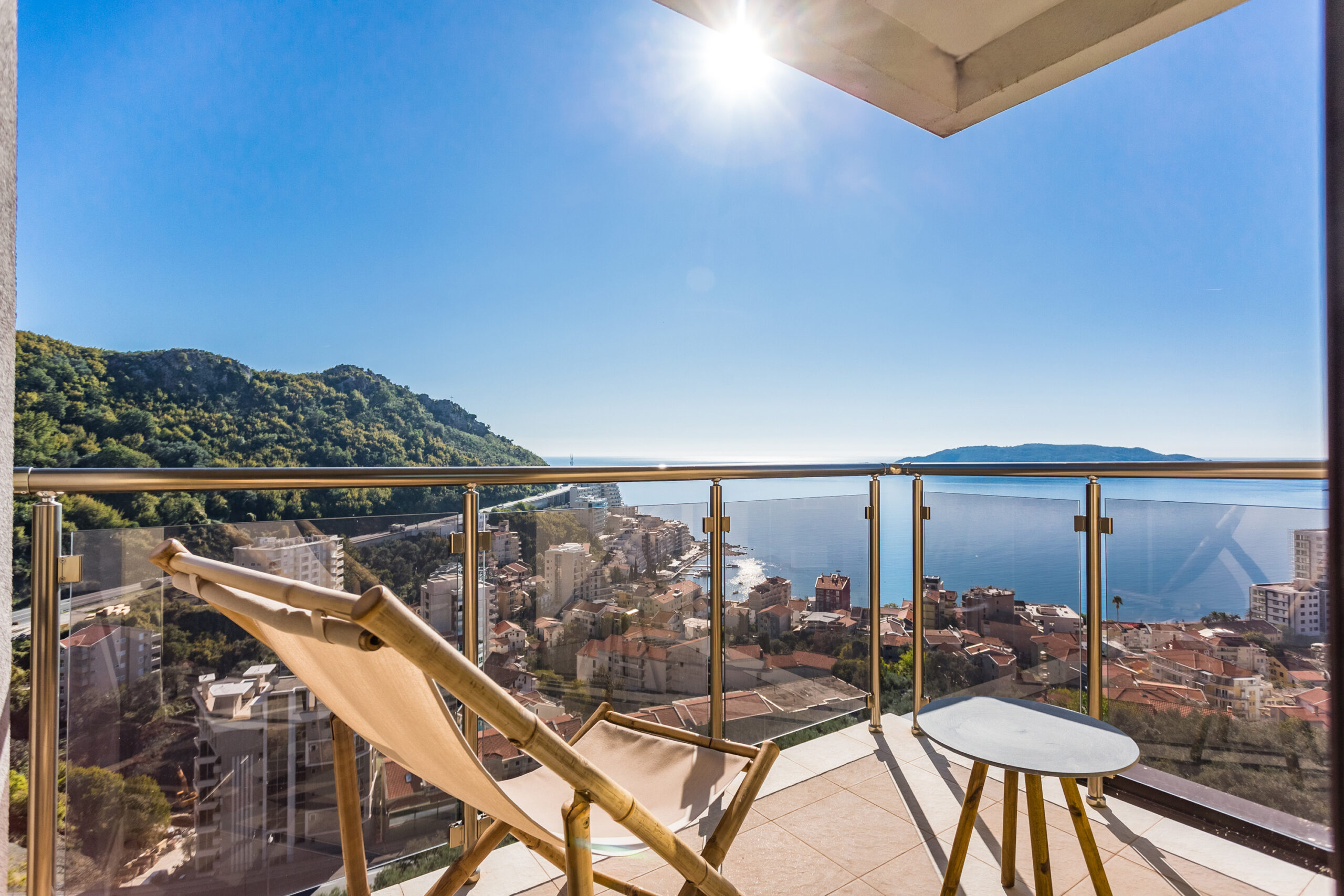 Penthouse balcony in Rafailovici, Montenegro: a sun lounger, a small table, and panoramic views of the sea, mountains, and the Budva coast.