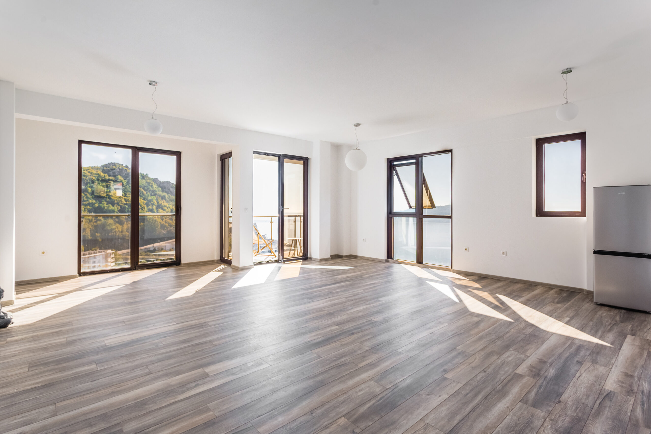 Bright living room in a penthouse, Rafailovici, Montenegro: panoramic windows with sea view, laminate flooring, and access to the terrace.