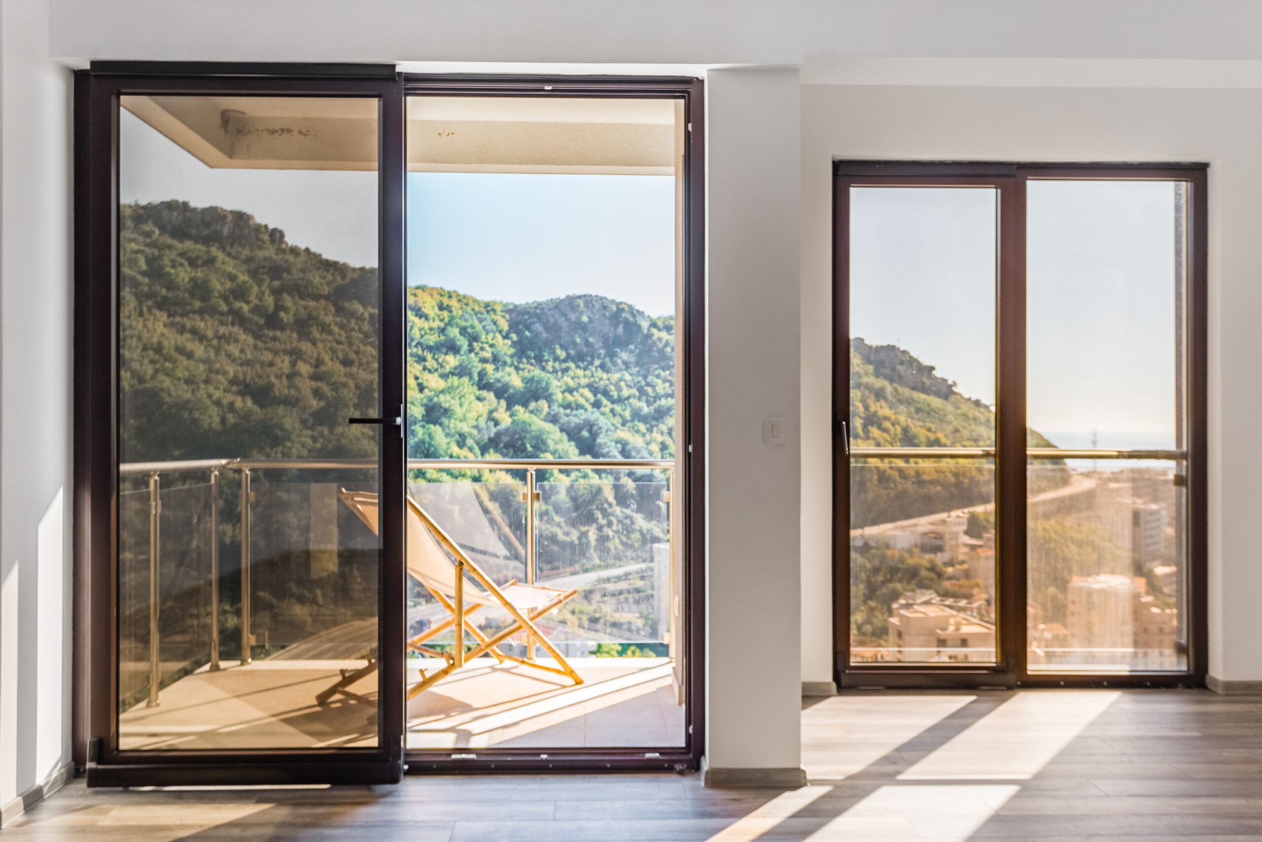 Living room in a penthouse in Rafailovici, Montenegro: panoramic windows, access to a balcony with mountain and sea views.