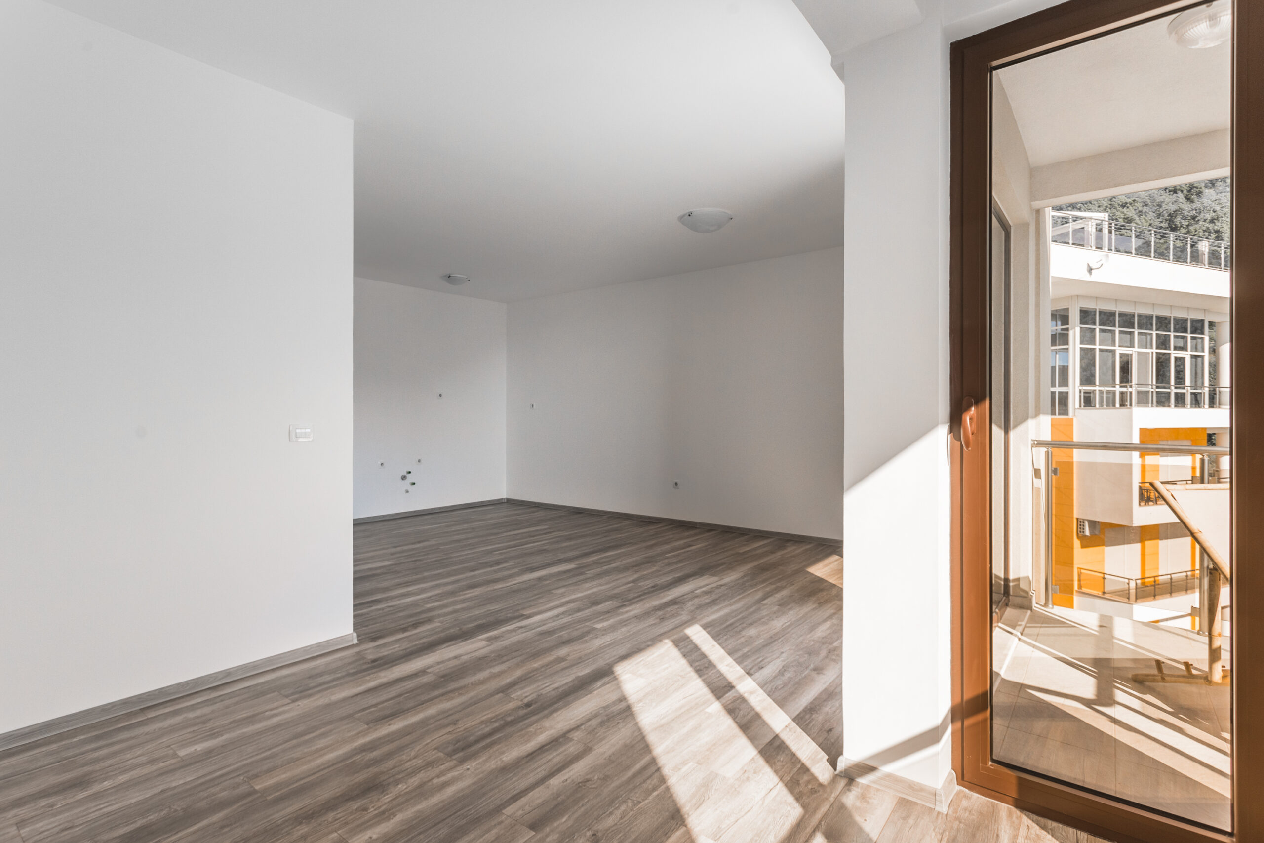 Bright living room with laminate flooring in a penthouse, Rafailovici, Montenegro, access to a terrace overlooking neighboring buildings.