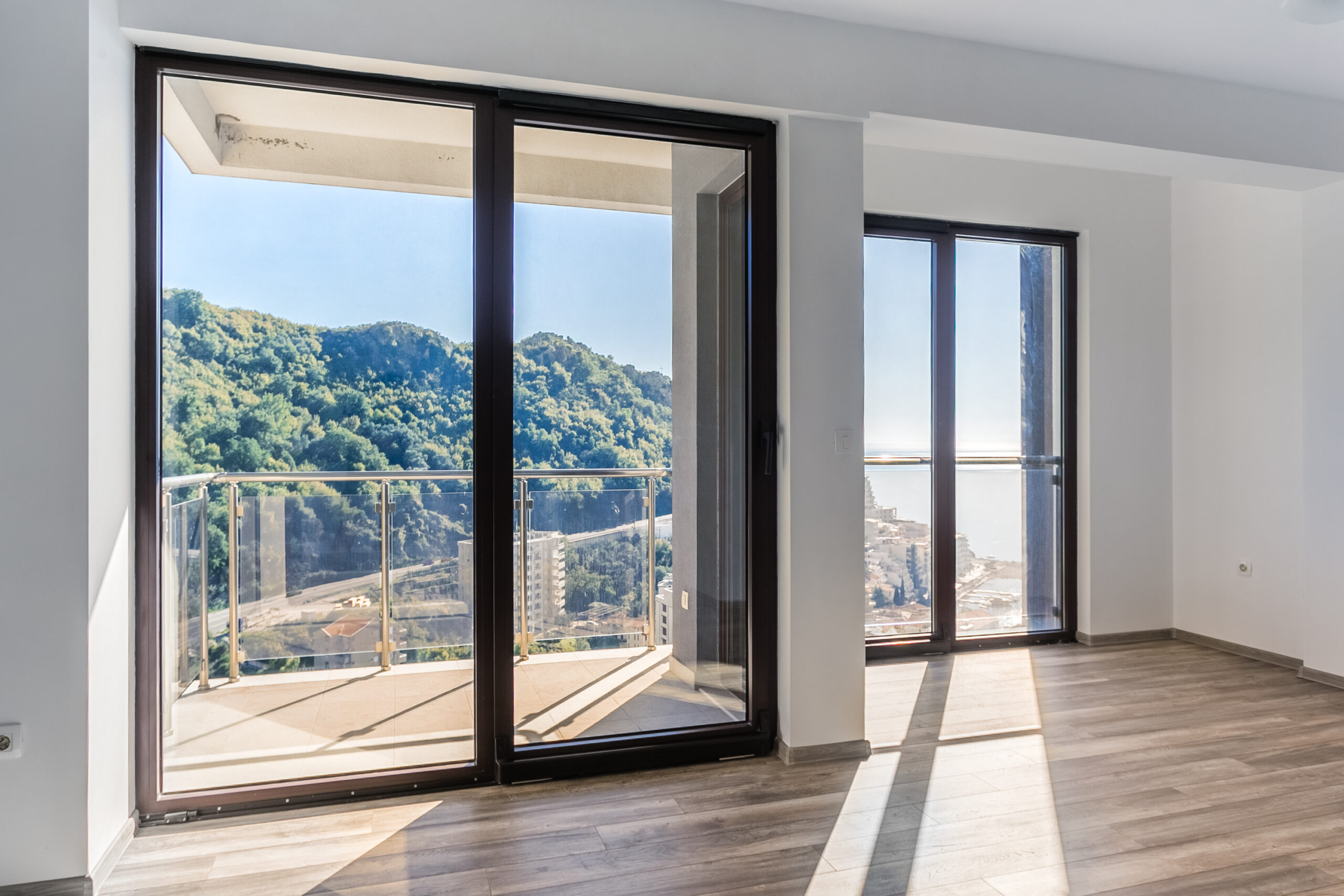 Bright living room in a penthouse in Rafailovići, Montenegro, with panoramic windows, a terrace, and sea and mountain views.