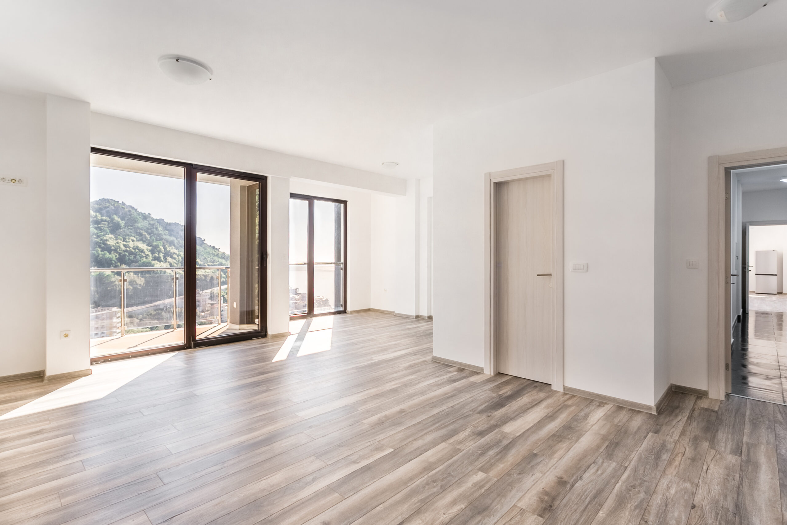 Bright living room in a penthouse, Rafailovici, Montenegro: panoramic windows, mountain and sea views, laminate flooring, modern style.
