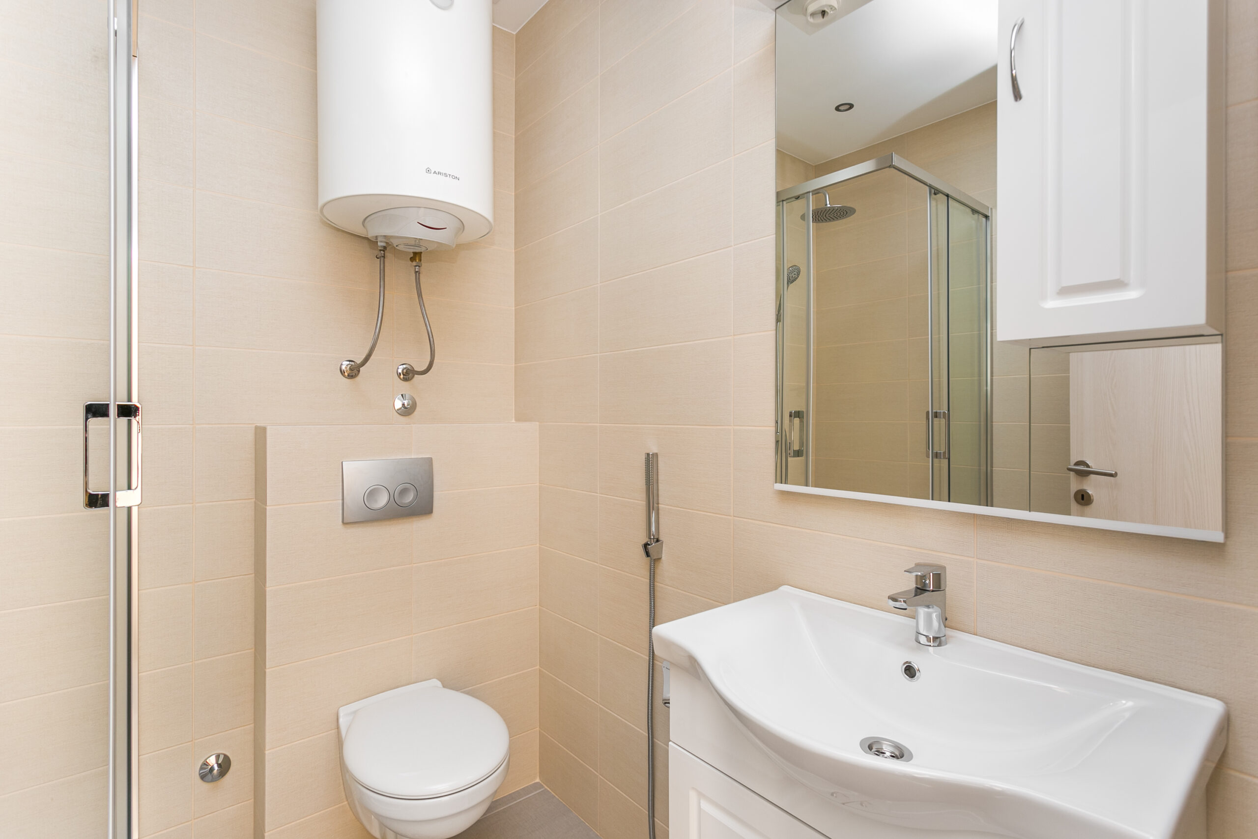 Modern bathroom in an apartment, Rafailovichi, Montenegro: shower cabin, Ariston water heater, and light-colored tiles.