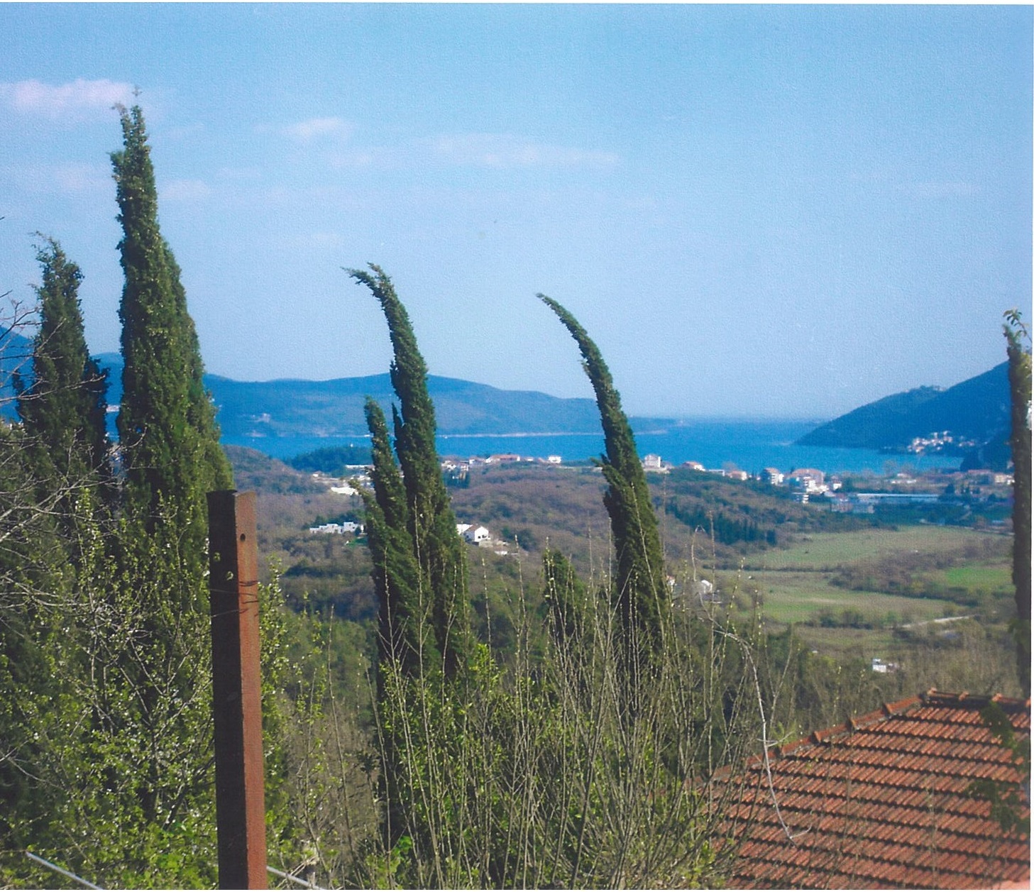 Panoramic view of the sea and mountains from a plot of land in Lučići, Herceg Novi, Montenegro: cypress trees and a tiled roof.