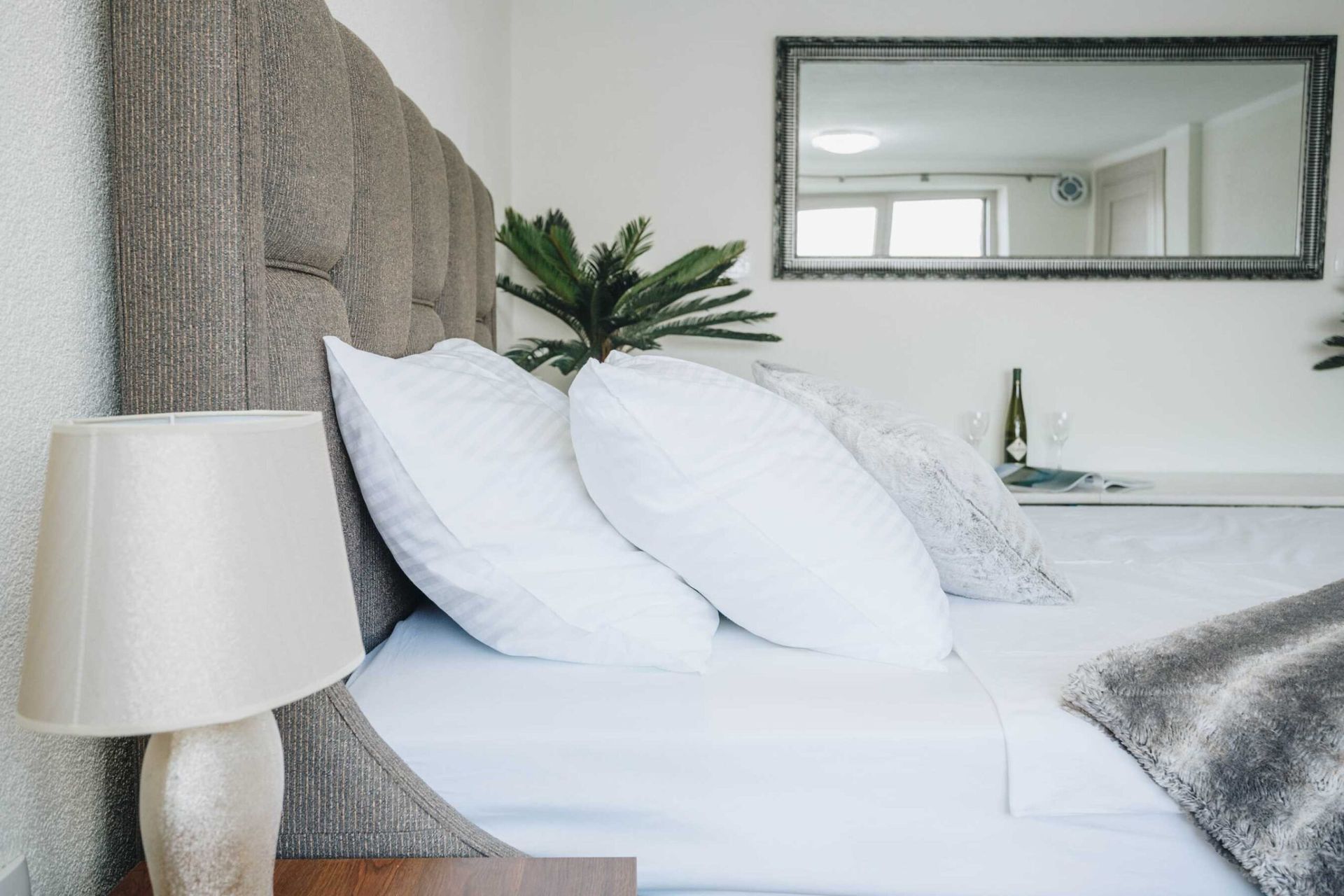 Cozy bedroom in a villa in Krašići, Montenegro: a double bed with a padded headboard, a table lamp, and a mirror.