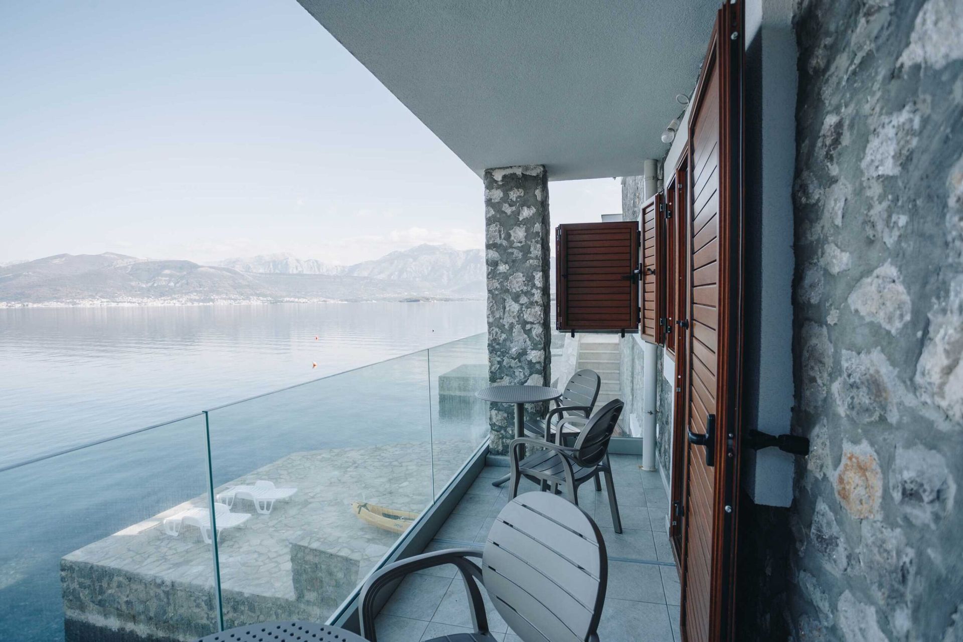 Balcony of a villa in Krašići, Montenegro: sea view, stone finish, glass railing, and outdoor furniture.