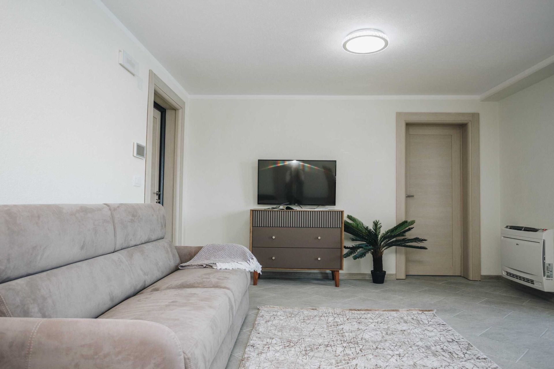Bright living room with a gray sofa and TV area in a villa in Krašići, Montenegro: modern interior with tiled flooring.