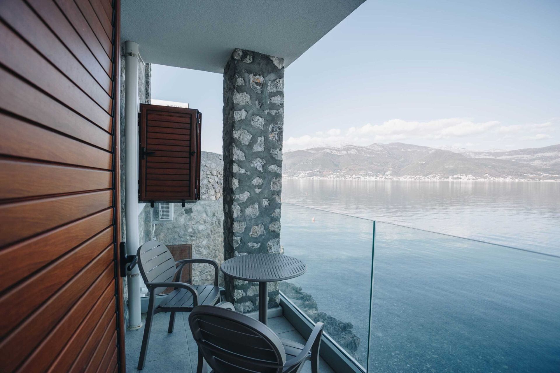 Villa balcony in Krašići, Montenegro: sea view, stone finish, glass railing, and a table with chairs.