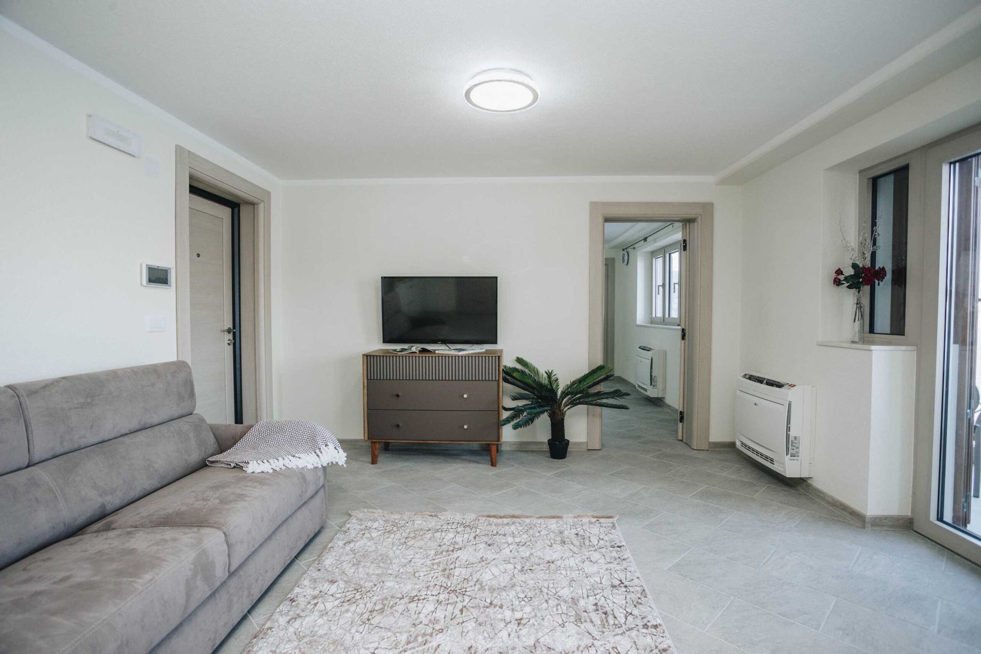 Bright living room with a gray sofa and dresser in a villa in Krašići, Montenegro: modern interior with tiled flooring.