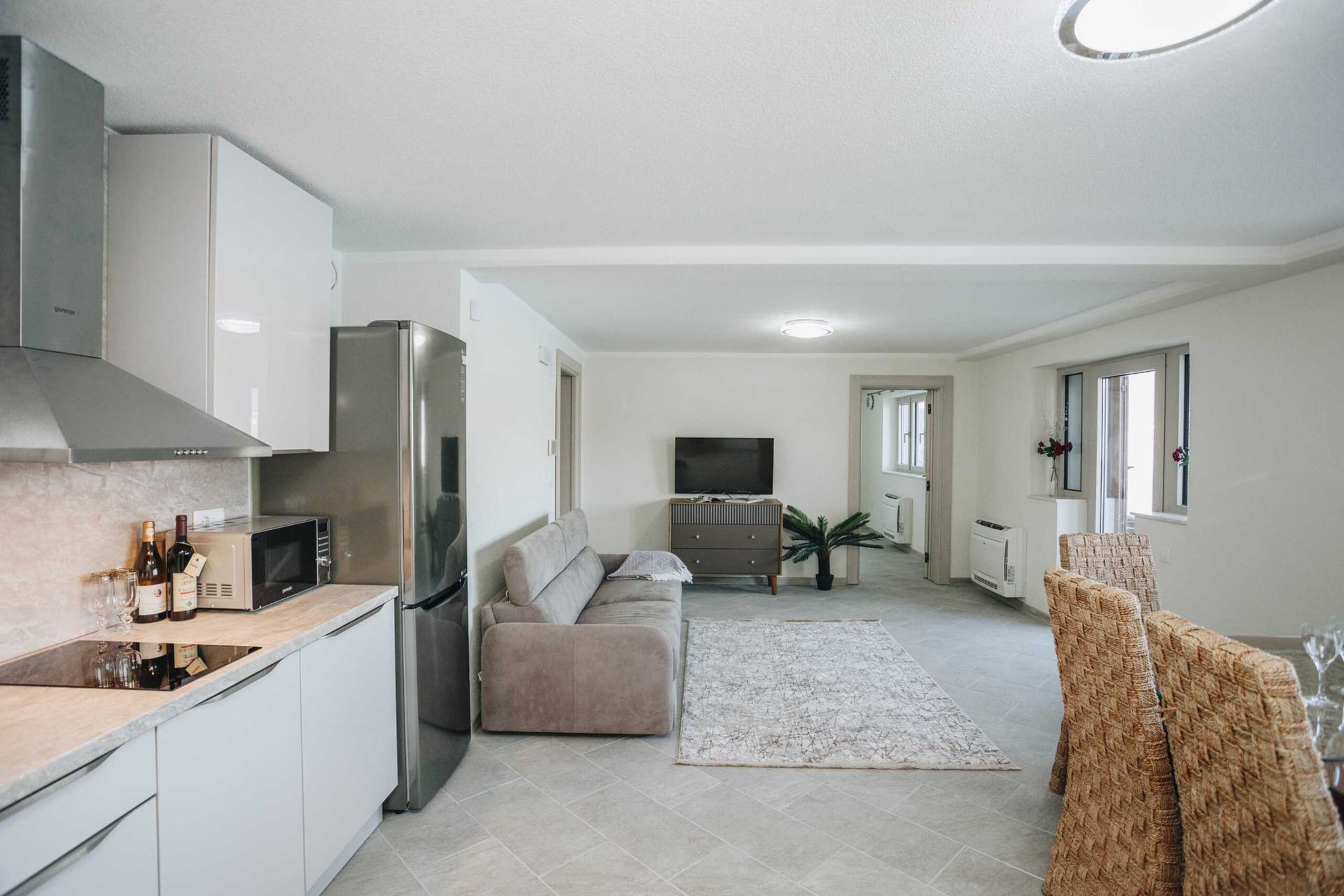 Modern living room with kitchen in a villa in Krašići, Montenegro: bright interior, soft sofa, and wicker furniture.