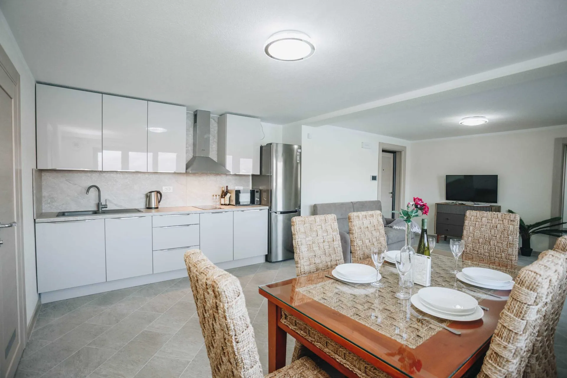 Modern kitchen with white cabinets, stainless steel fridge, and a dining table set with woven chairs.