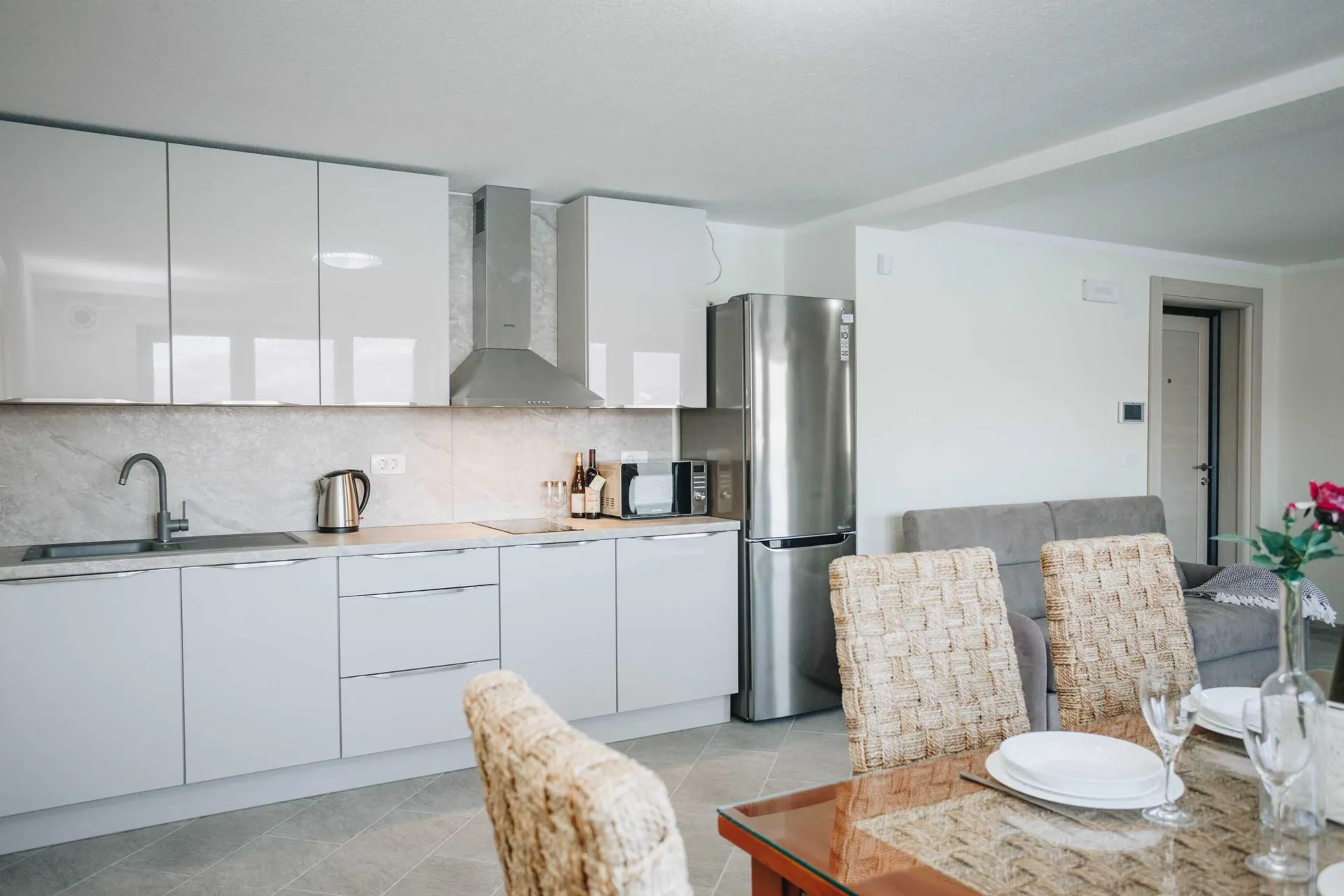 Modern kitchen with glossy white cabinets, stainless steel fridge, and a dining table with woven chairs.