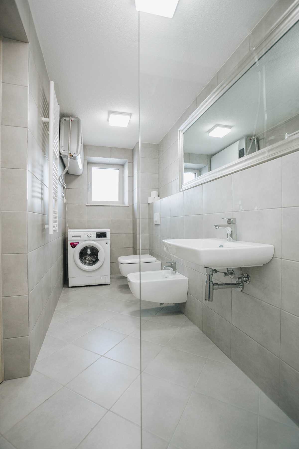 Modern bathroom with a shower and washing machine in a villa in Krašići, Montenegro. Light-colored tiles and fixtures.