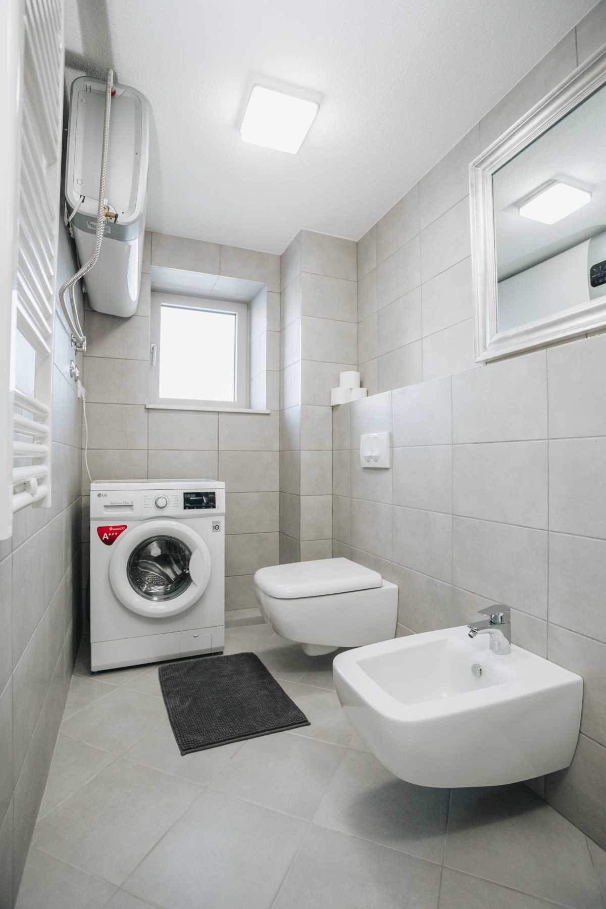 Modern bathroom with a bidet and washing machine in a villa in Krašići, Montenegro. Light tiles and sanitary ware.
