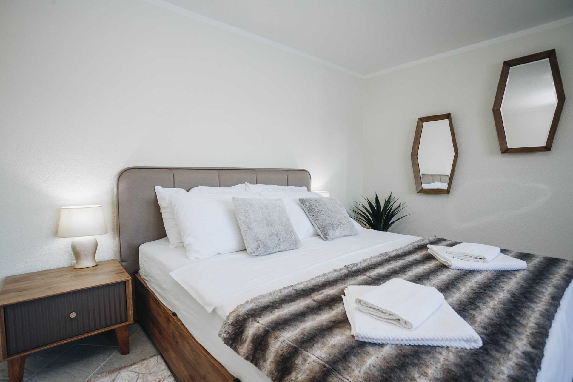 Cozy bedroom in a villa in Krašići, Montenegro: a double bed, a wooden nightstand, and stylish mirrors on the wall.