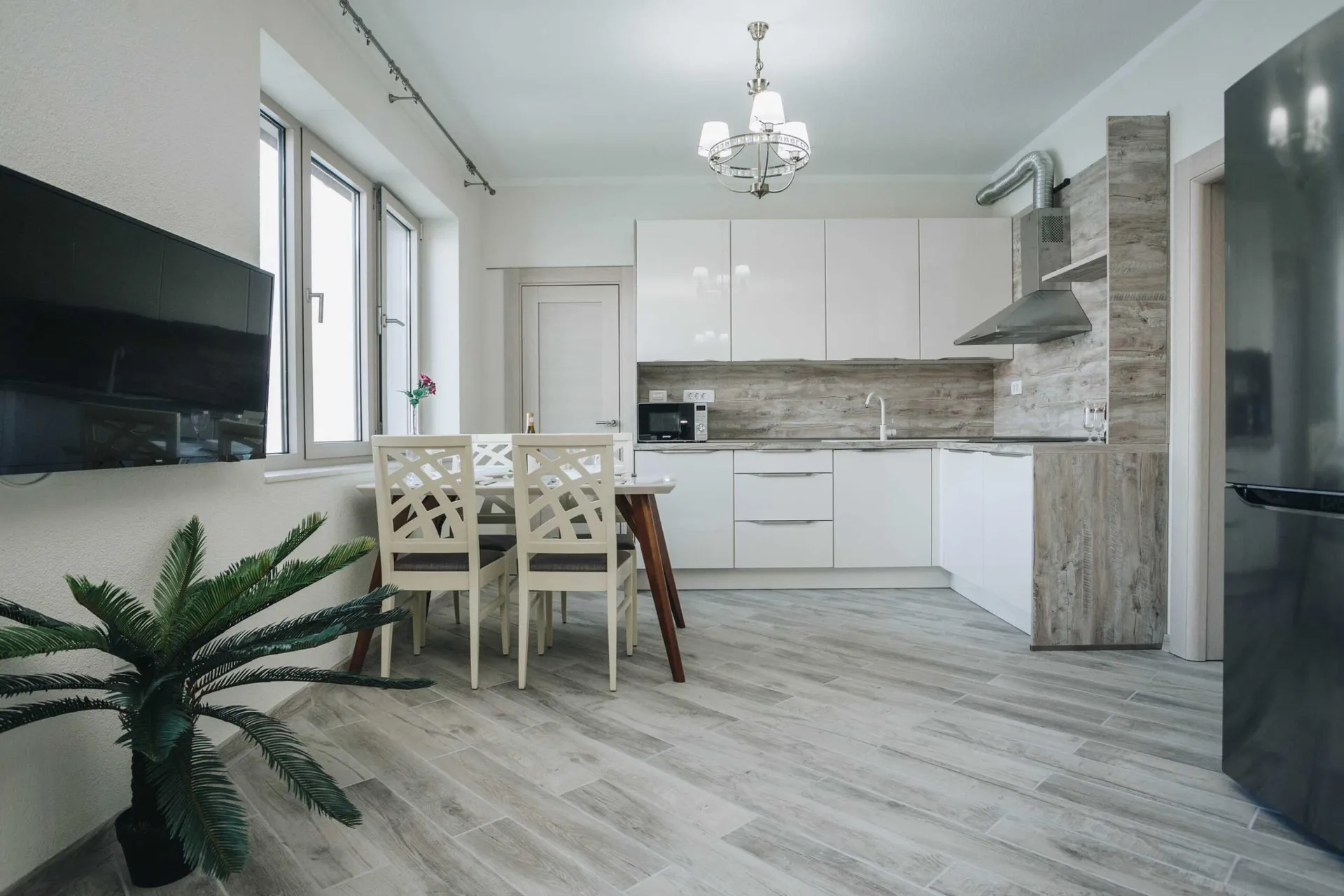 Modern kitchen with white cabinets, wood backsplash, dining table set, and black refrigerator visible.