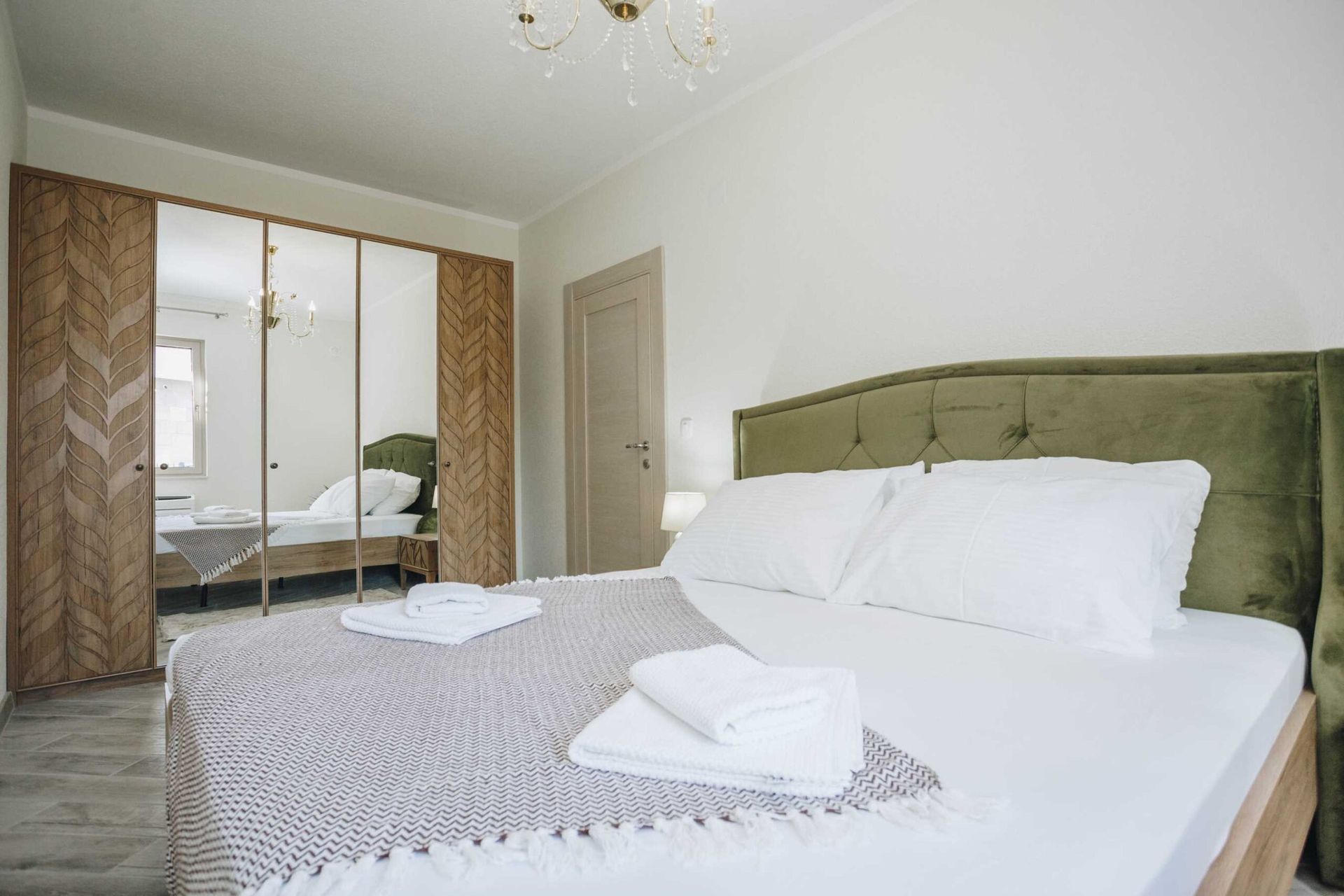 Bedroom in a villa in Krašići, Montenegro: a double bed with a green headboard and a mirrored sliding wardrobe.