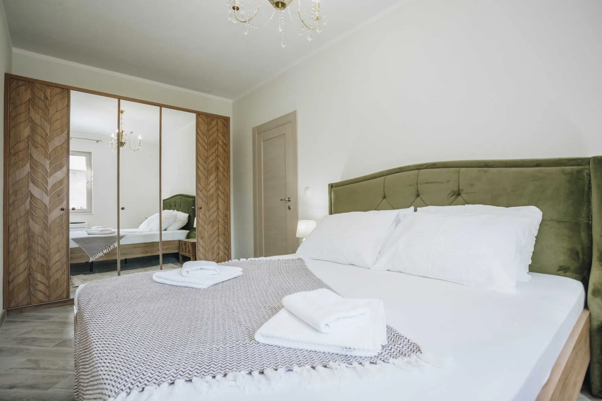 Bedroom featuring a large bed with a green headboard, wooden wardrobe with mirrored doors, and a crystal chandelier.