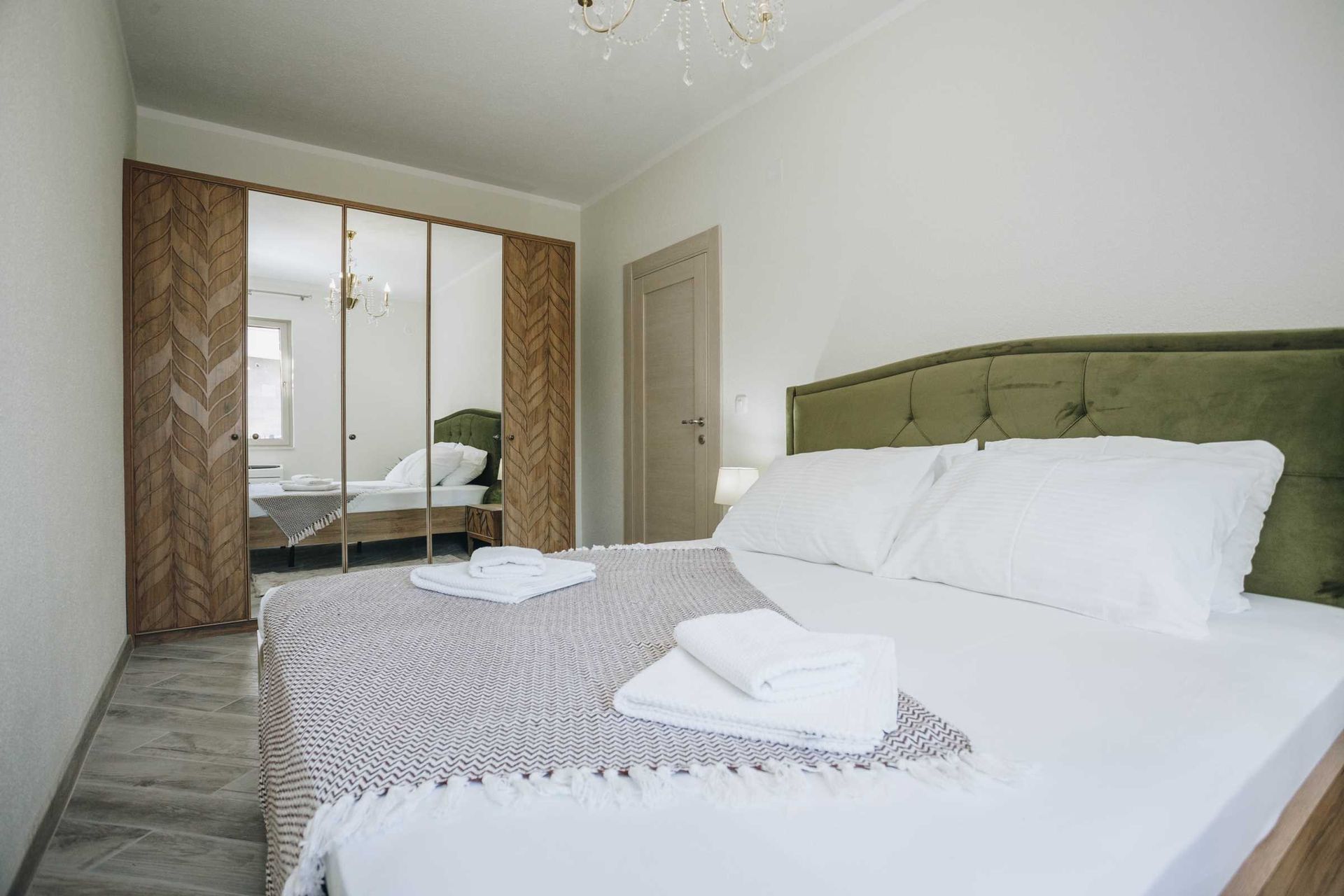 Bedroom in a villa in Krašići, Montenegro: a double bed with a green headboard and a mirrored sliding wardrobe.