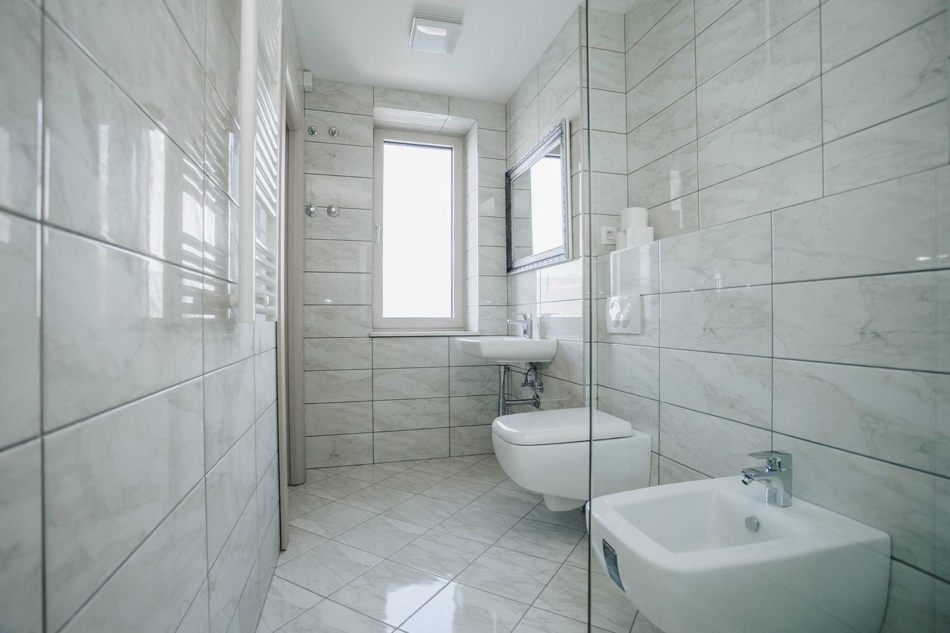 Modern bathroom with a shower cabin and bidet in a villa in Krašići, Montenegro, finished with light marble-look tiles.