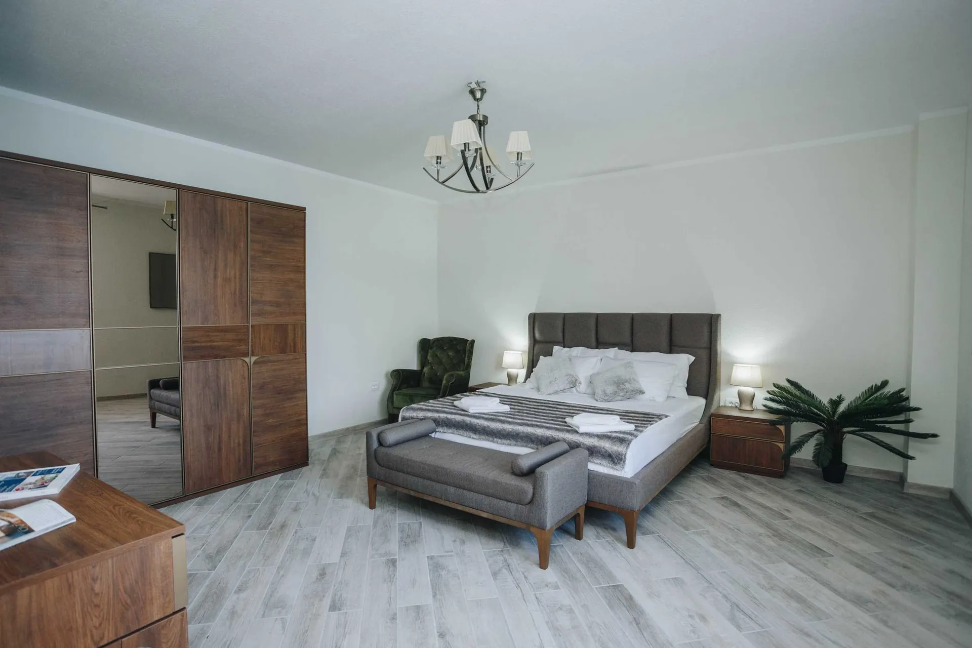 Modern bedroom featuring a large bed with gray headboard, wooden wardrobe with mirror, and bench at foot.