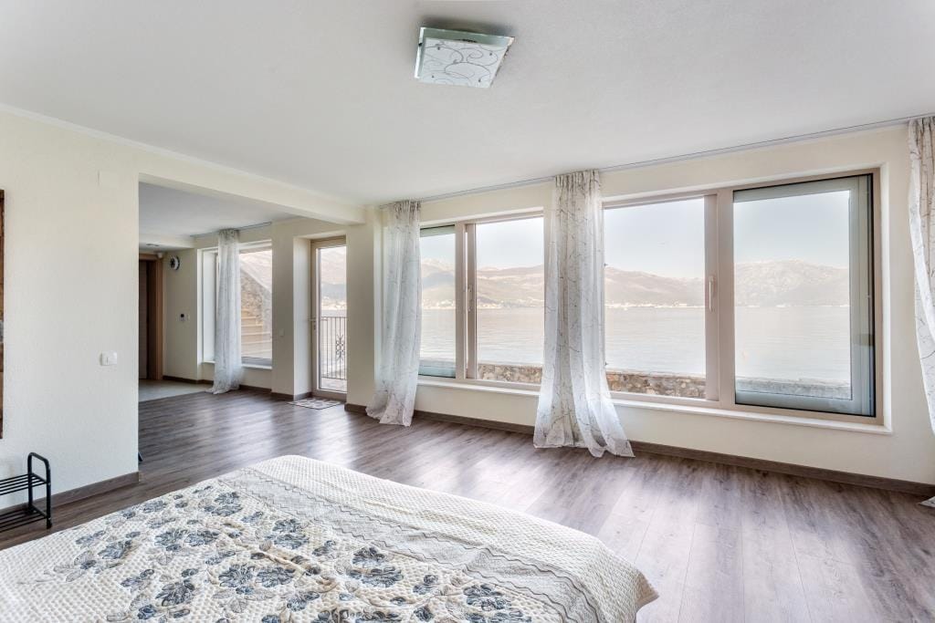 Bedroom with panoramic windows and sea view in a villa in Krašići, Montenegro: bright interior, laminate flooring, and access to the terrace.