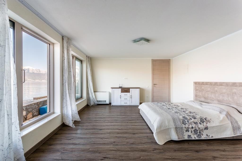 Bright bedroom in a villa in Krašići, Montenegro, with a double bed, dresser, and panoramic sea and mountain views.
