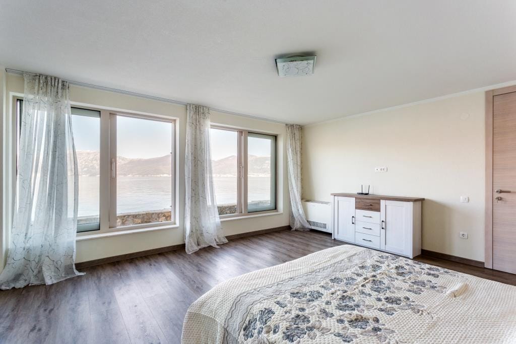 Bedroom with panoramic sea view in a villa, Krašići, Montenegro: bright interior, double bed, and dresser.