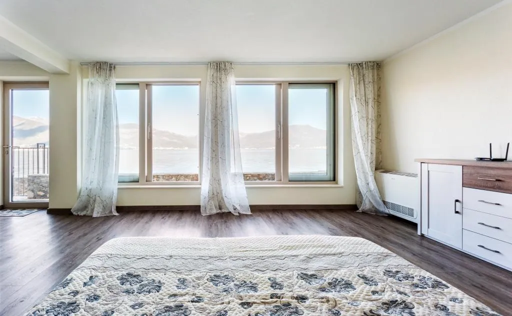 Bedroom with a bed, dresser, and large windows overlooking water and mountains.